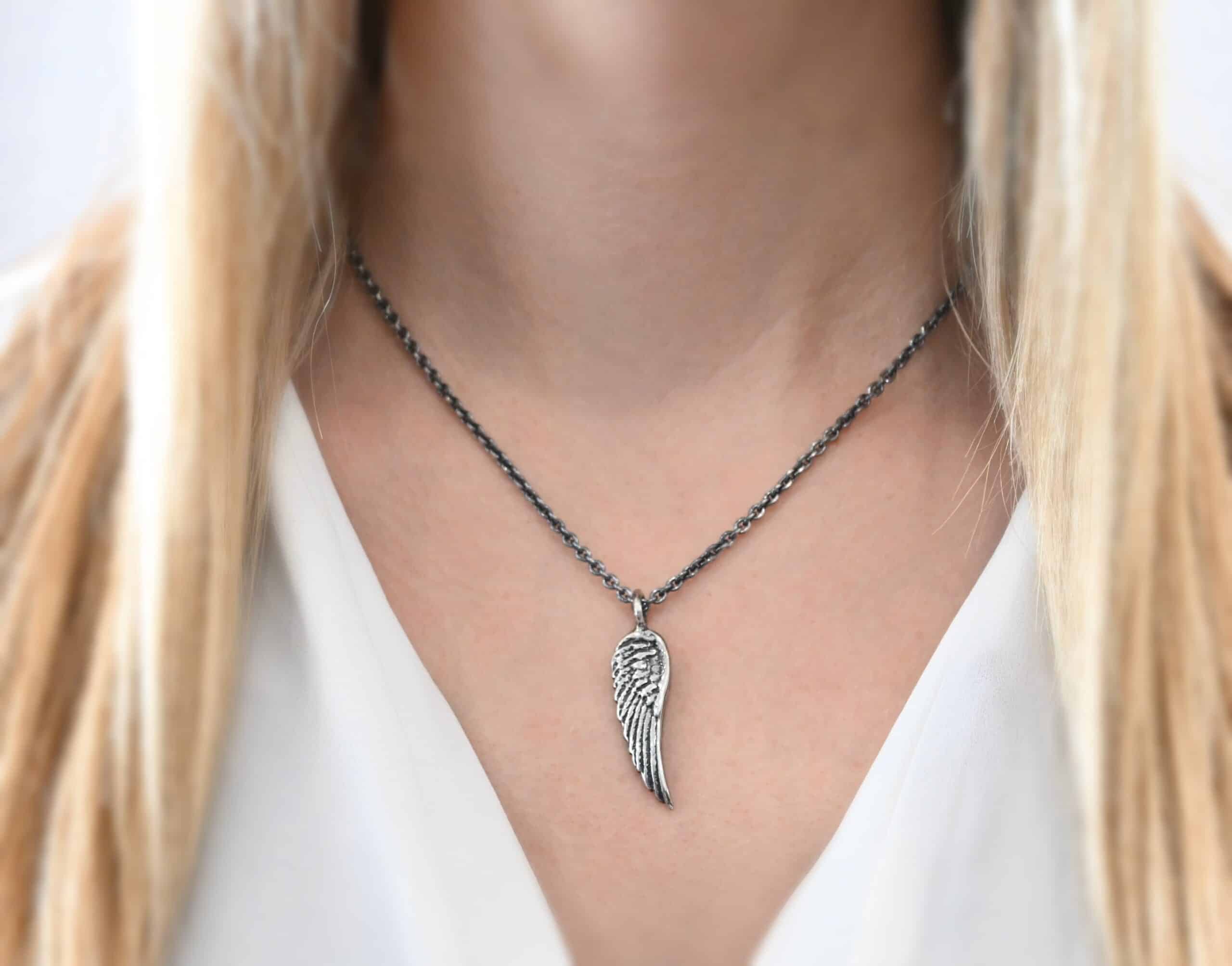 Angel Kiss Necklace Photo of the "Angel Kiss" Necklace. Made out of sterling silver. There is a medium sized angel wing pendant with a loop soldered to the top. There is a chain going through the charm. Necklace is worn by a model.
