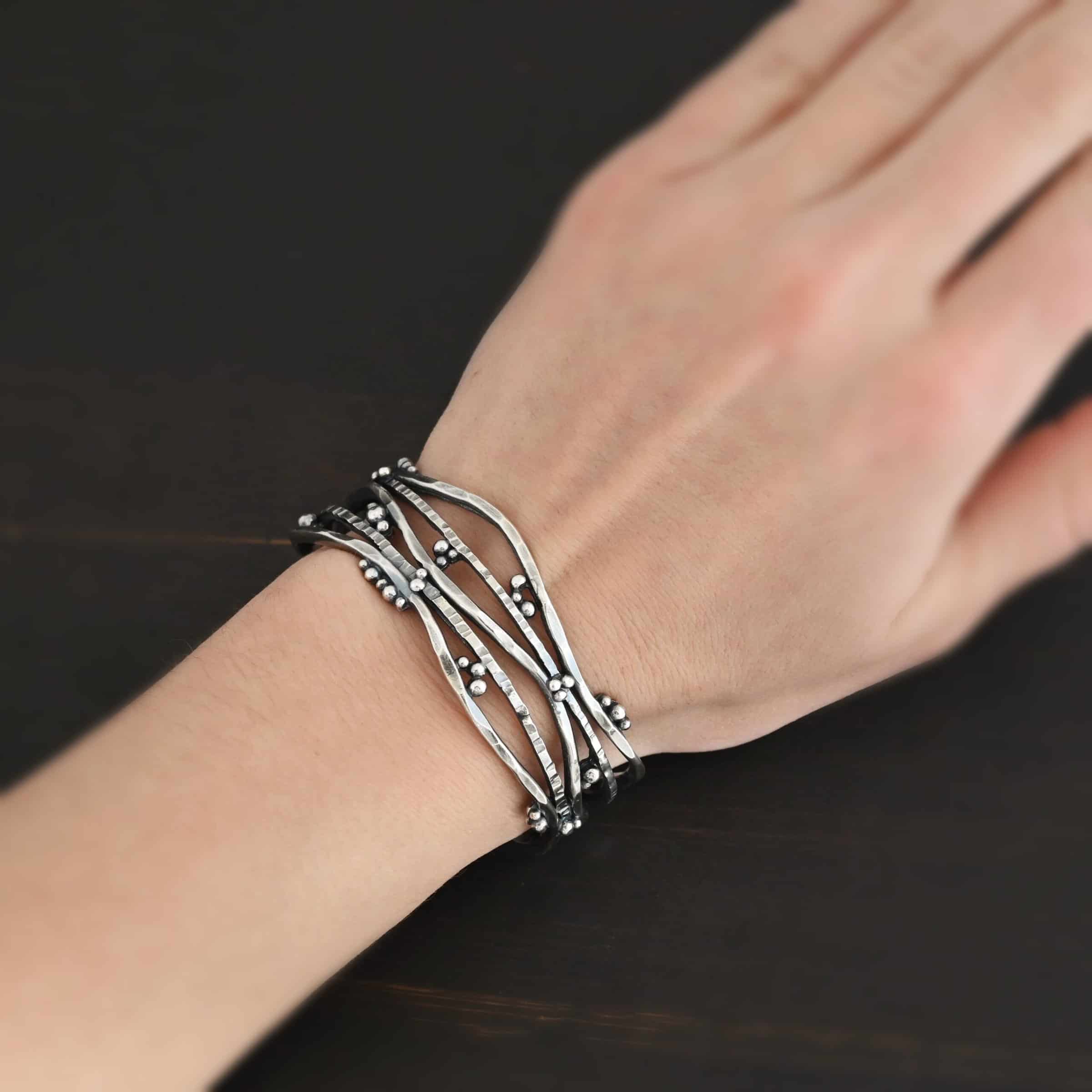 Wild Prairie Cuff Photo of the "Wild Prairie" Cuff. Made out of sterling silver. Cuff is made out of multiple thick, hammered lines of wavy silver. The silver connects at different points, throughout the cuff, but it all connects at the very back to create the cuff. There is silver ball detail around the entire cuff. Cuff is worn by a model to demonstrate size.