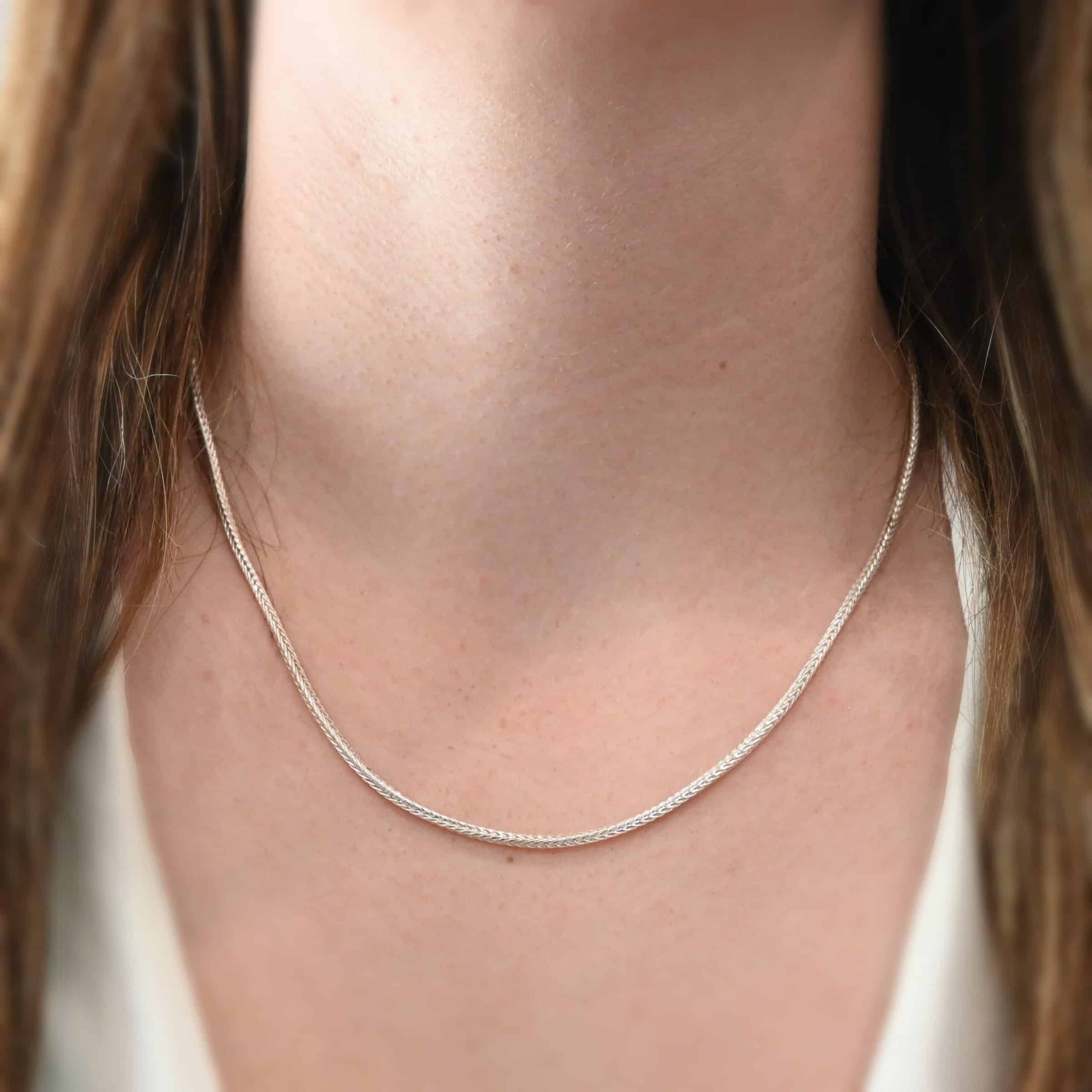 "Snake Foxtail" Chain as shown on a model. Chain is shiny and 18 inches long. Chain is a 2mm foxtail chain. Model is wearing a white v-neck shirt.
