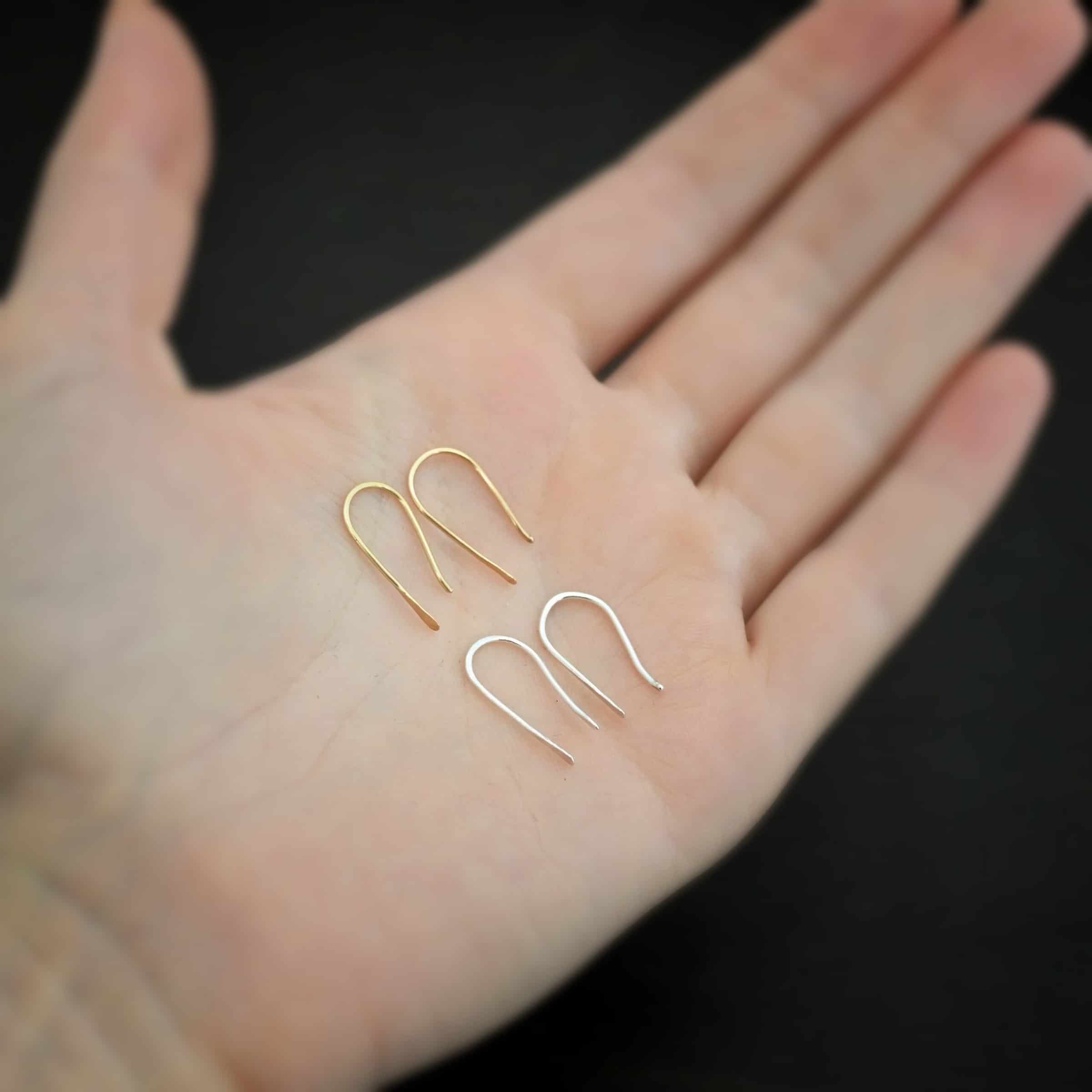 Roadies Photo of the "Roadie" Earrings. Made out of 14k gold and sterling silver. Earrings are very simple. They are an ear wire with one end lightly hammered and tipped and the other end of the earring is a hammered paddle. Earrings are lying against a dark background. The 14k gold pair is on top and the silver pair beneath it. Earrings are lying in the palm of a hand.