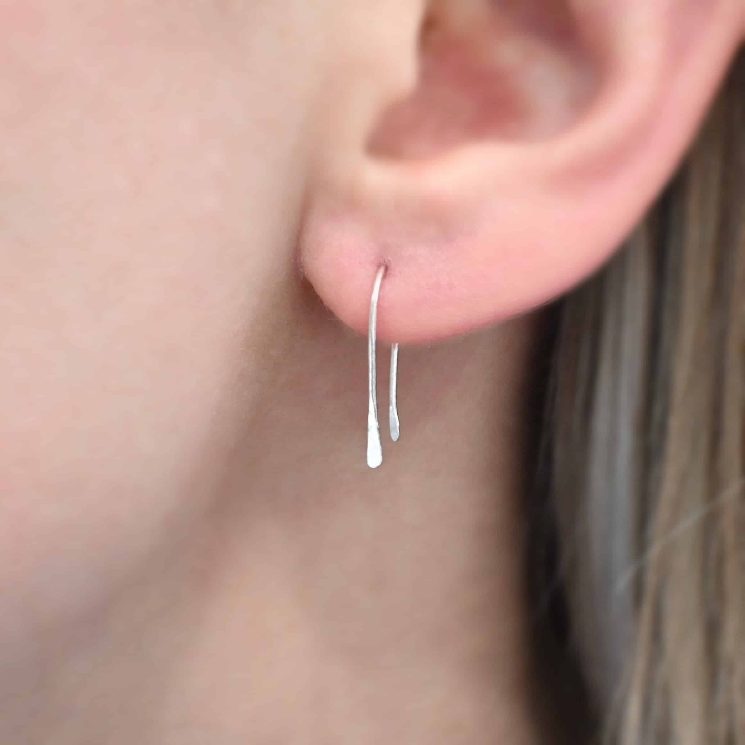 Roadies Photo of the "Roadie" Earring shown up close by a model. Made out of sterling silver. Earrings are very simple. They are an ear wire with one end lightly hammered and tipped and the other end of the earring is a hammered paddle.