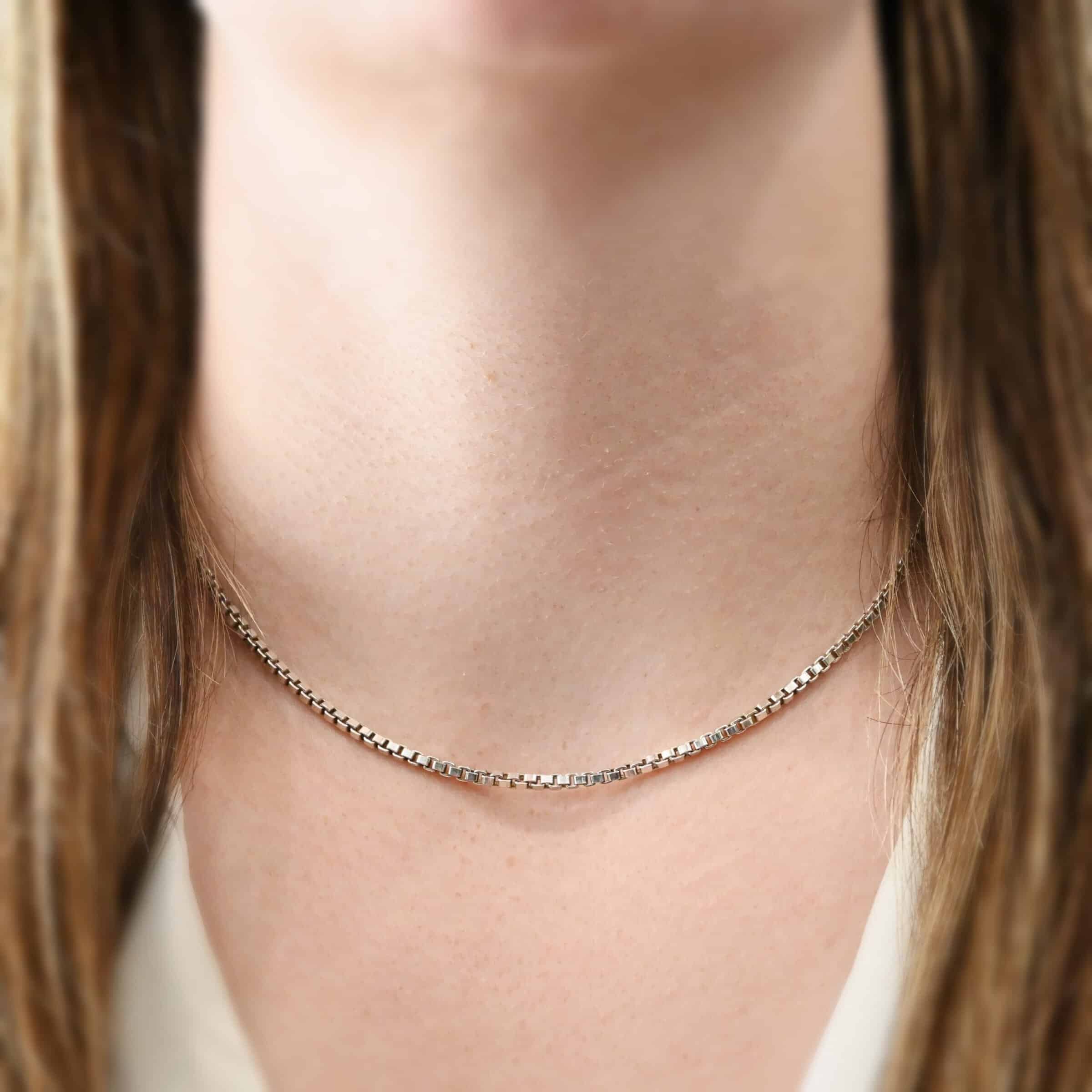 Close up of the "Briggs Box" Chain as shown on a model. Chain is shown at 16" long and shiny. This is a heavy box chain with links that are 2.5mmx1.4mm. Model is wearing a white v-neck shirt.