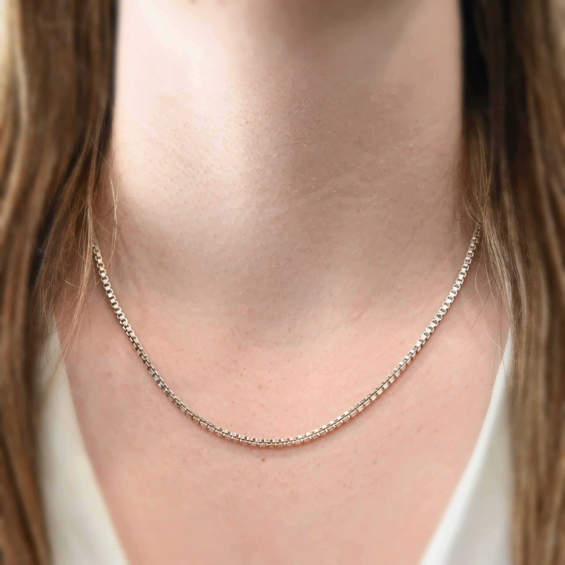 Close up of the "Briggs Box" Chain as shown on a model. Chain is shown at 18" long and shiny. This is a heavy box chain with links that are 2.5mmx1.4mm. Model is wearing a white v-neck shirt.