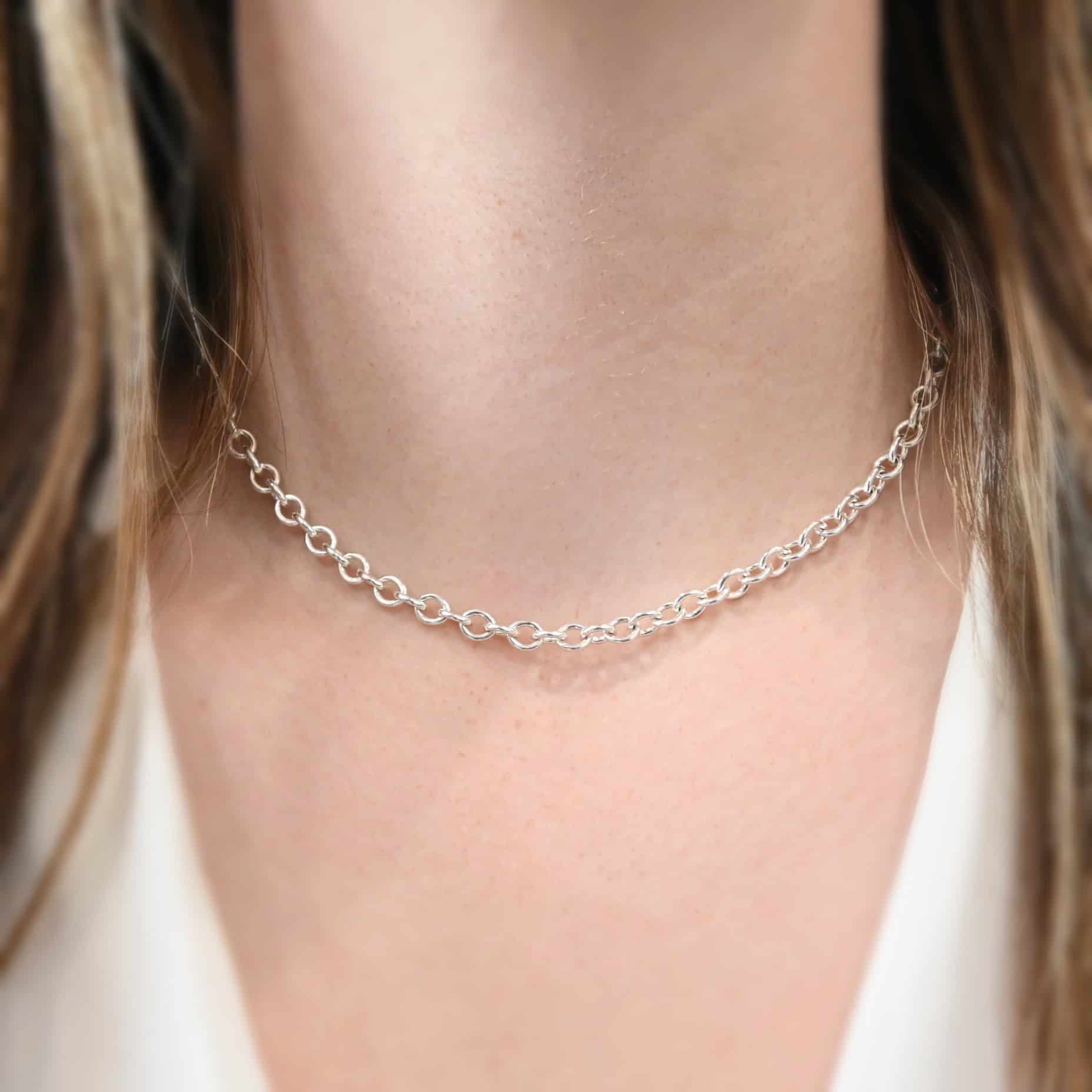 Close up of the "Joy" Chain as shown on a model. Chain is 16 inches long and shiny. Model is wearing a white v-neck shirt. Links are heavy oval links measure 6.5×5.4mm.