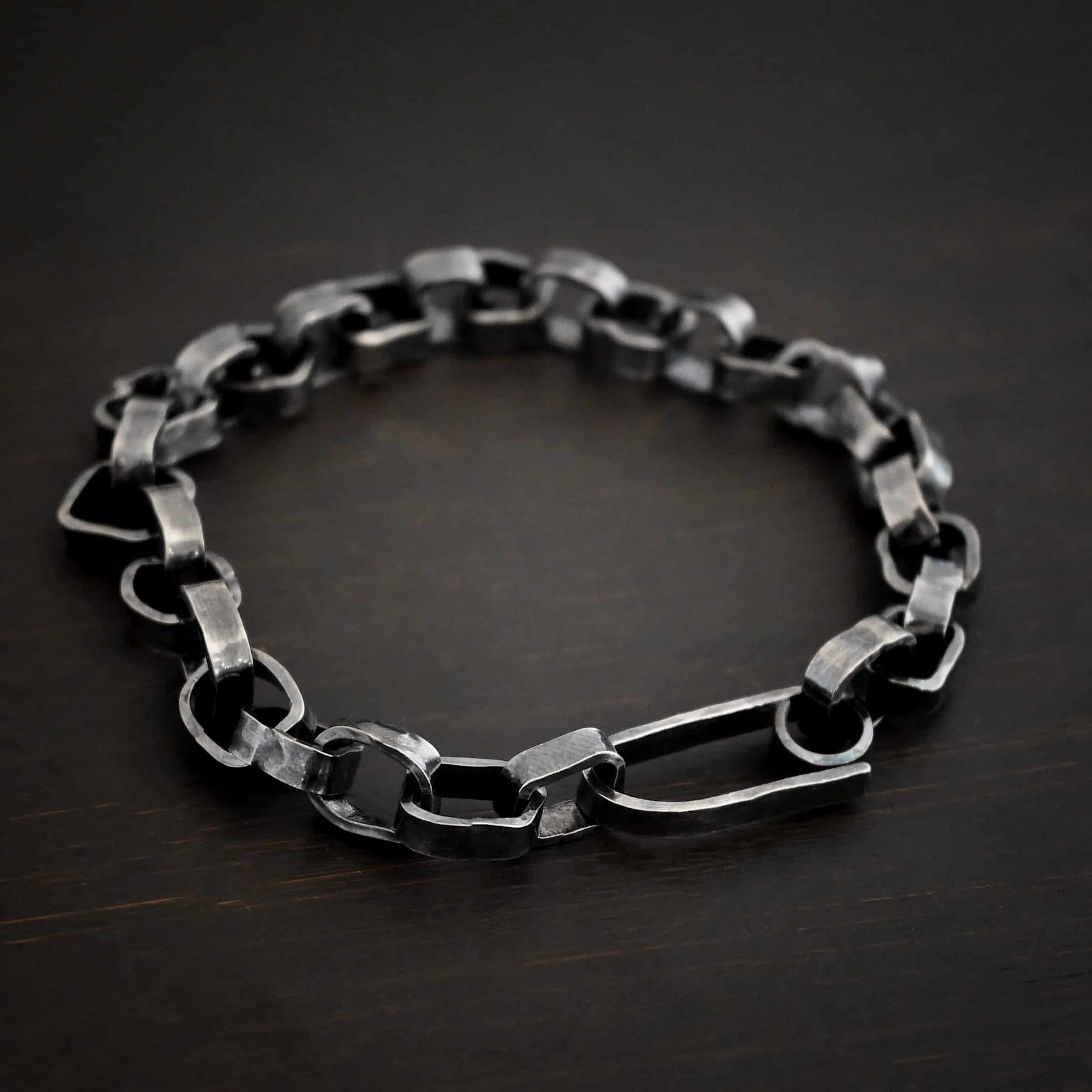 Rustic Bracelet Photo of the "Rustic" Bracelet. Bracelet is made out of sterling silver. Each link is a thick circle link that is hammered and oxidized. The clasp of the bracelet is also thick, hammered, and oxidized, but it is a long oval shape. Bracelet is lying against a dark background.