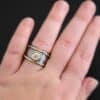 Photo of the "Banded Together" Ring. Made out of sterling silver, gold, and moissanite. The ring band does not fully connect. It is thick and hammered. There is a moissanite in the center that connects both sides. It is set in gold. There is a thin band of gold on top and on the bottom of the ring. They both go fully around and connect both sides of the ring as well. Ring is worn by a model.