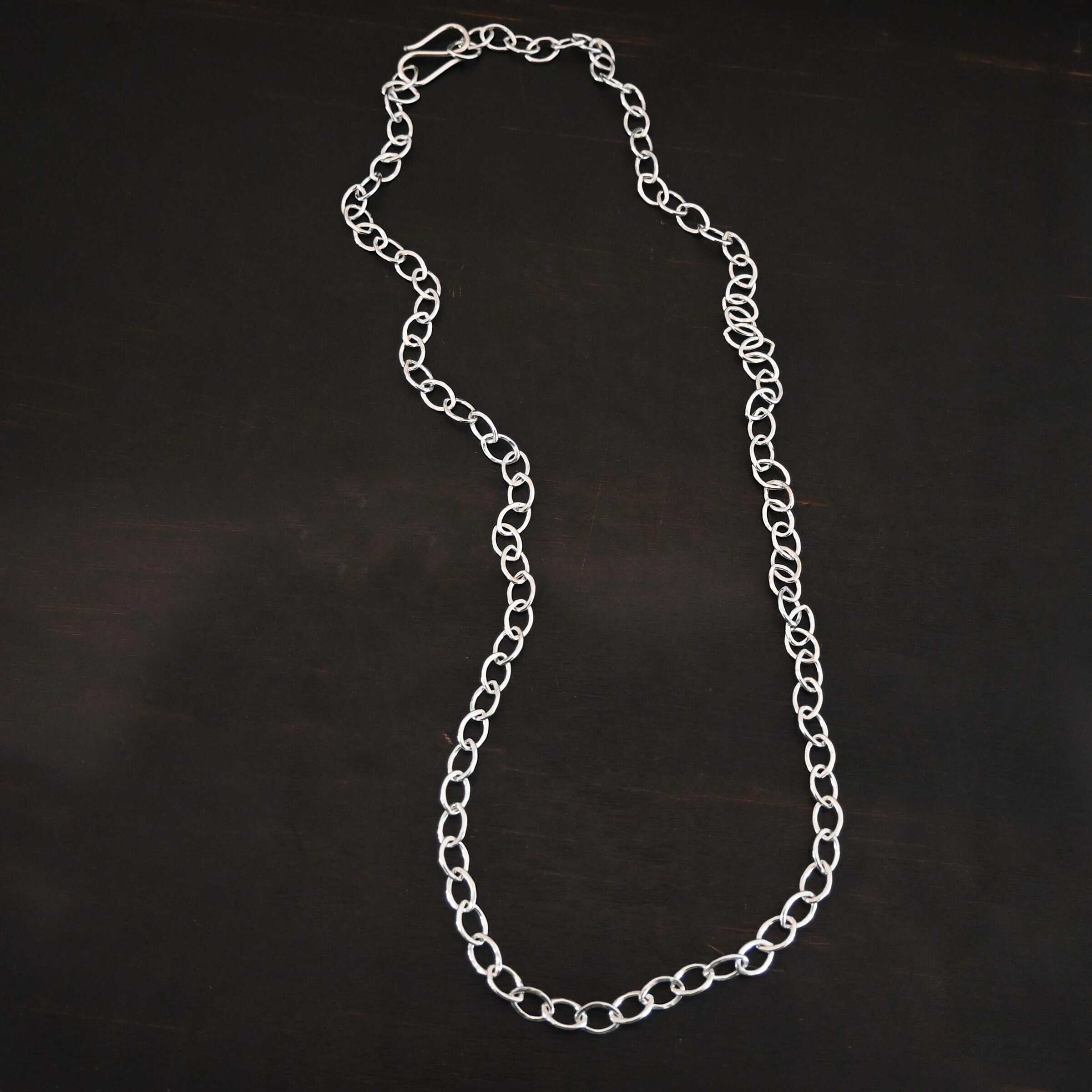 Sky Chain Hammered The "Sky" Chain. Shown as hammered, and shiny. Handmade links that are made out of sterling silver and connected to each other. Comes with a S hook clasp. Chain is laying against a dark background.