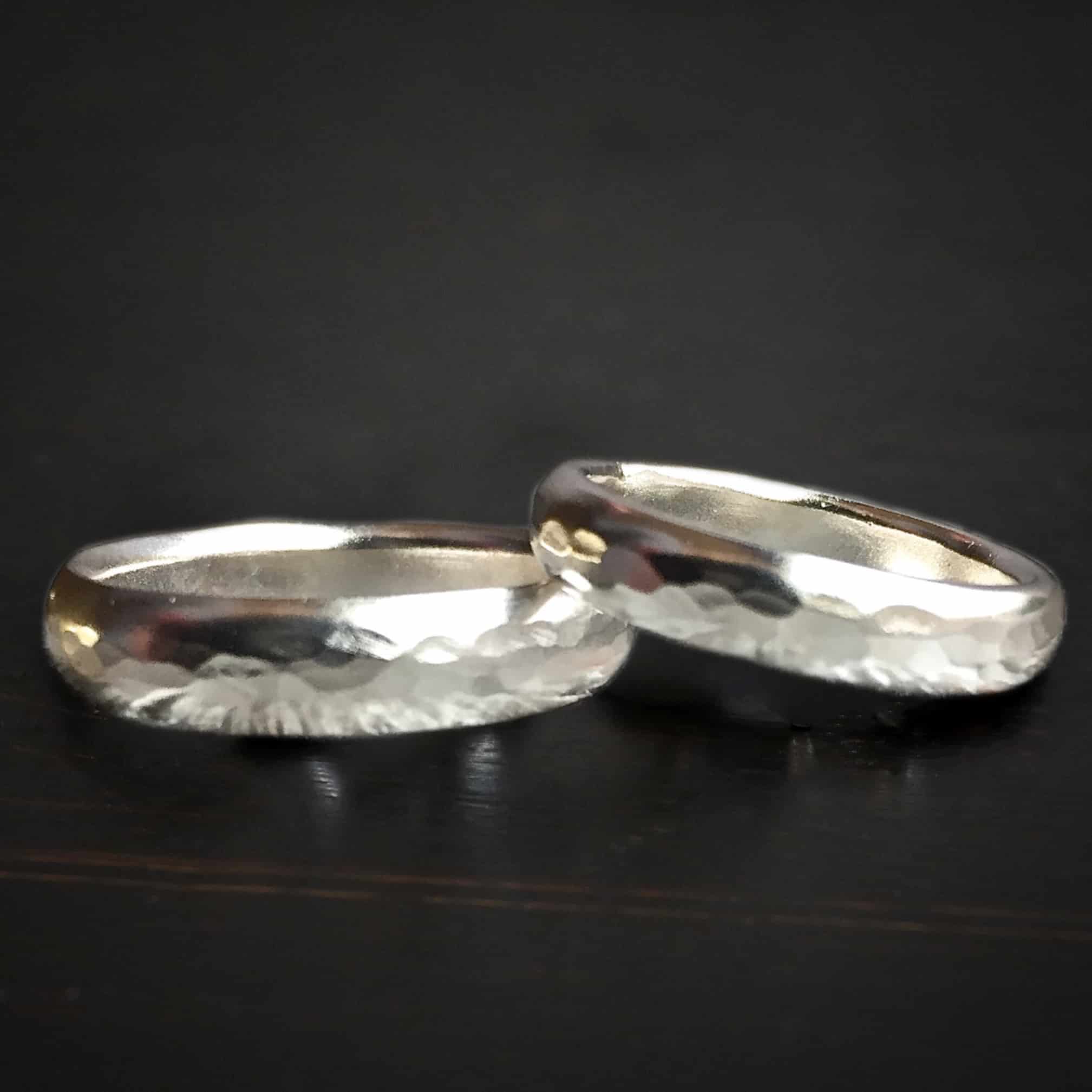 My Best Friend Wedding Band Photo of the "My Best Friend" Wedding Bands. They are both made out of shiny sterling silver and hammered. They are thicker bands of silver. One rests on top of the other. Both are lying against a dark background.