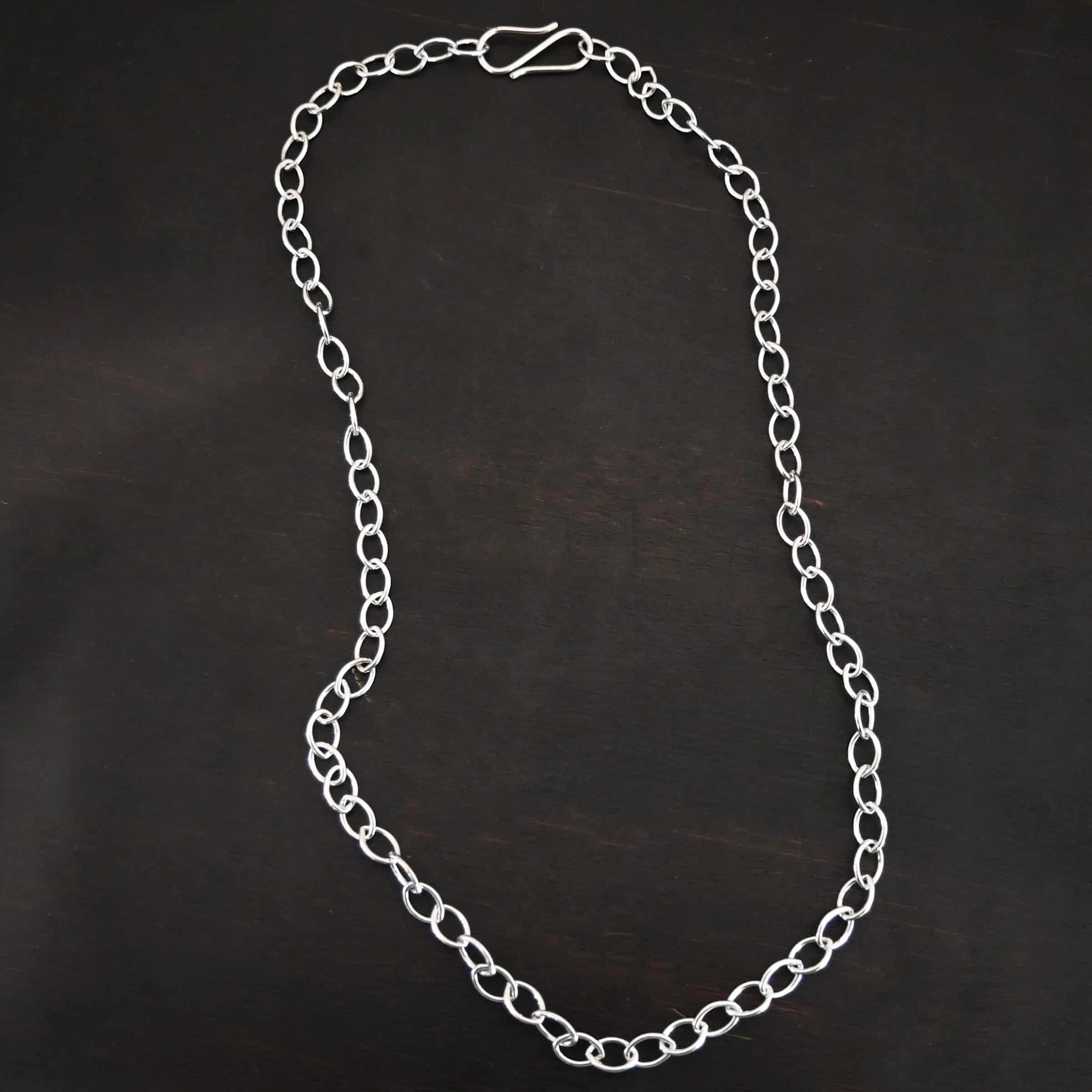 Sky Chain Smooth The "Sky" Chain. Shown as smooth, and shiny. Handmade links that are made out of sterling silver and connected to each other. Comes with a S hook clasp. Chain is laying against a dark background.