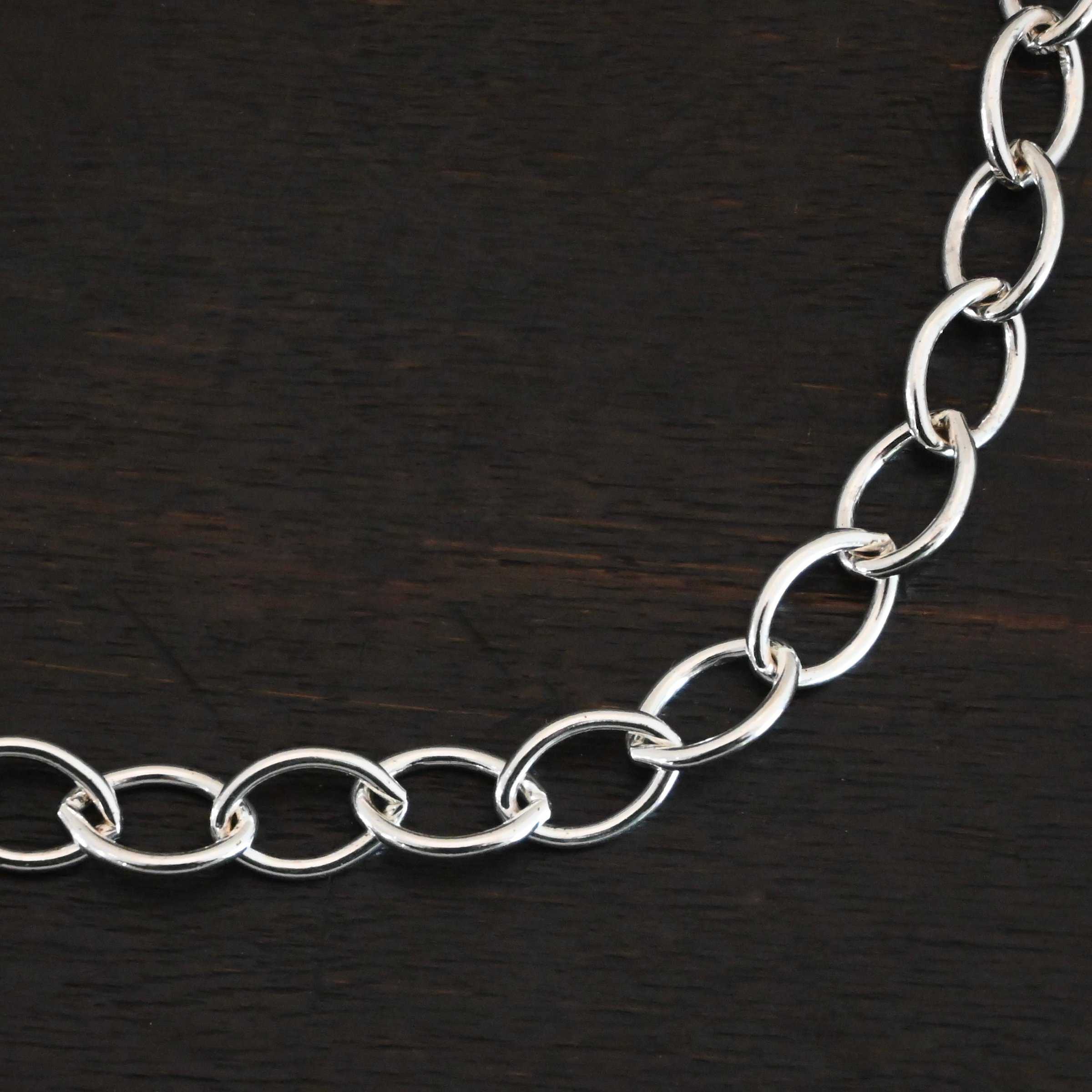Sky Chain Smooth The "Sky" Chain. Shown as smooth, and shiny. Handmade links that are made out of sterling silver and connected to each other. Chain is laying against a dark background.