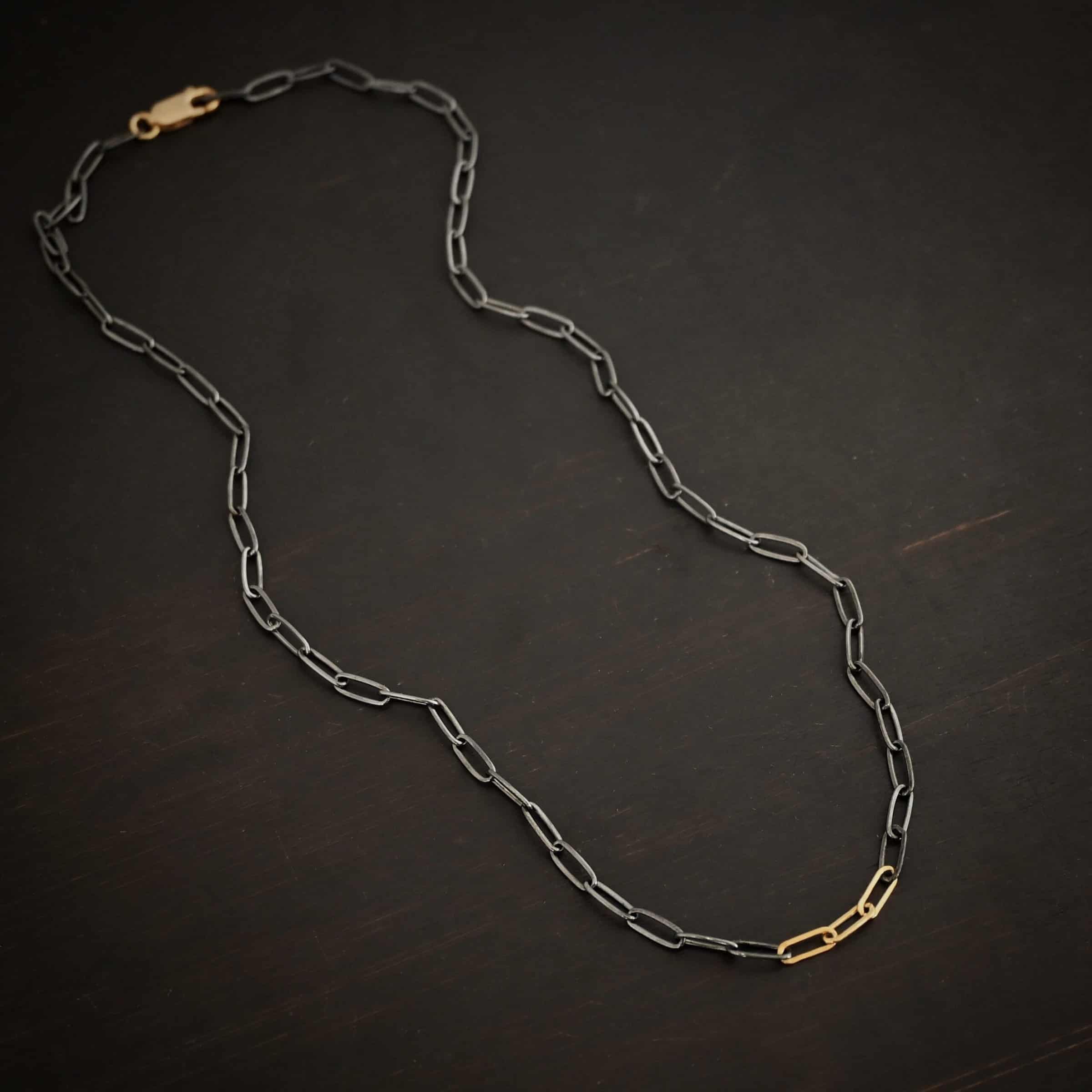 Lulu Link Silver & GF "Lulu Link" Chain as shown as oxidized and gold filled. Links are 8.5x3x2mm. Chain is lying against a dark background.
