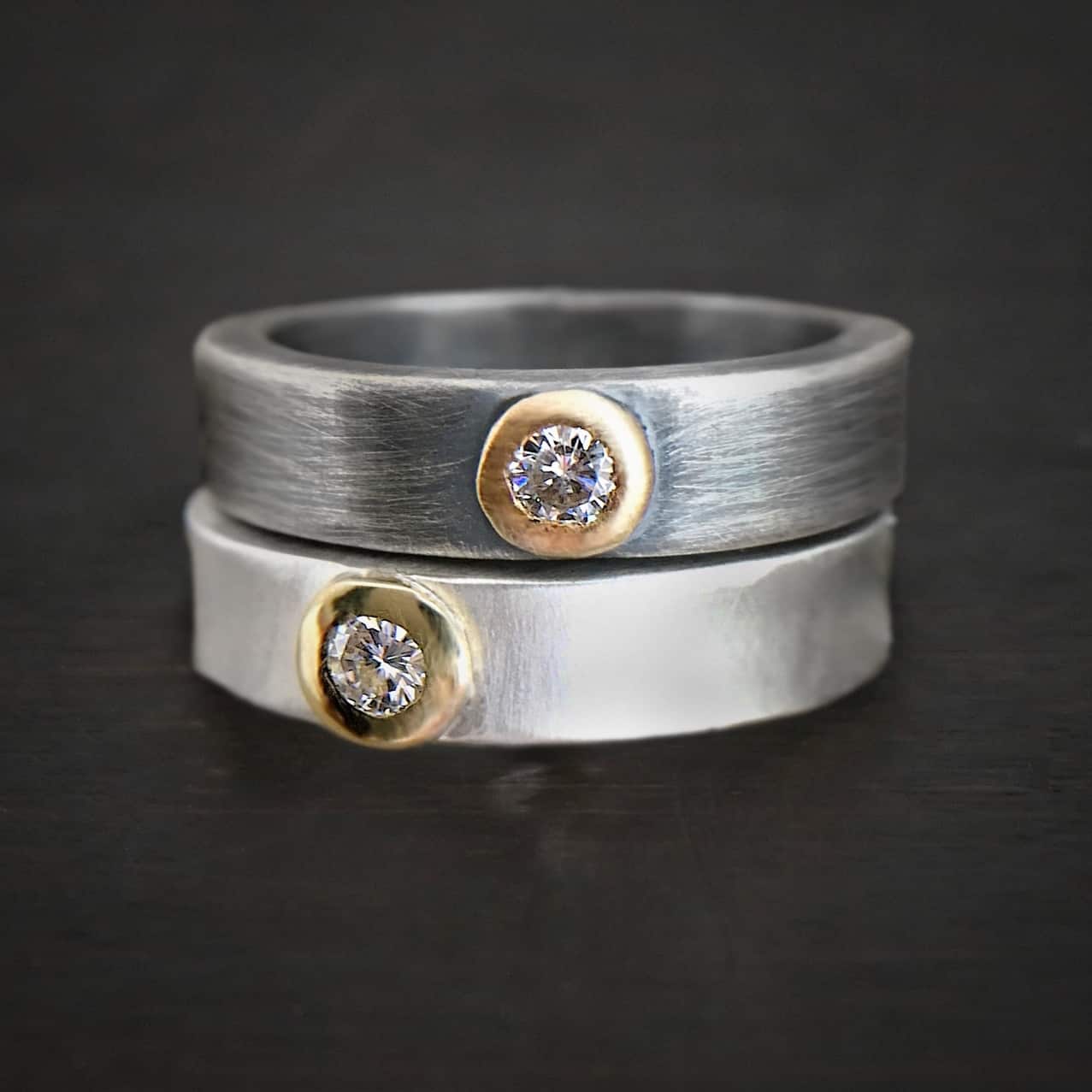 Photo of the "Adoration" Rings. Each ring has a small diamond in the center that is set in gold. The top ring is oxidized and brushed lightly, and the bottom ring is shiny.