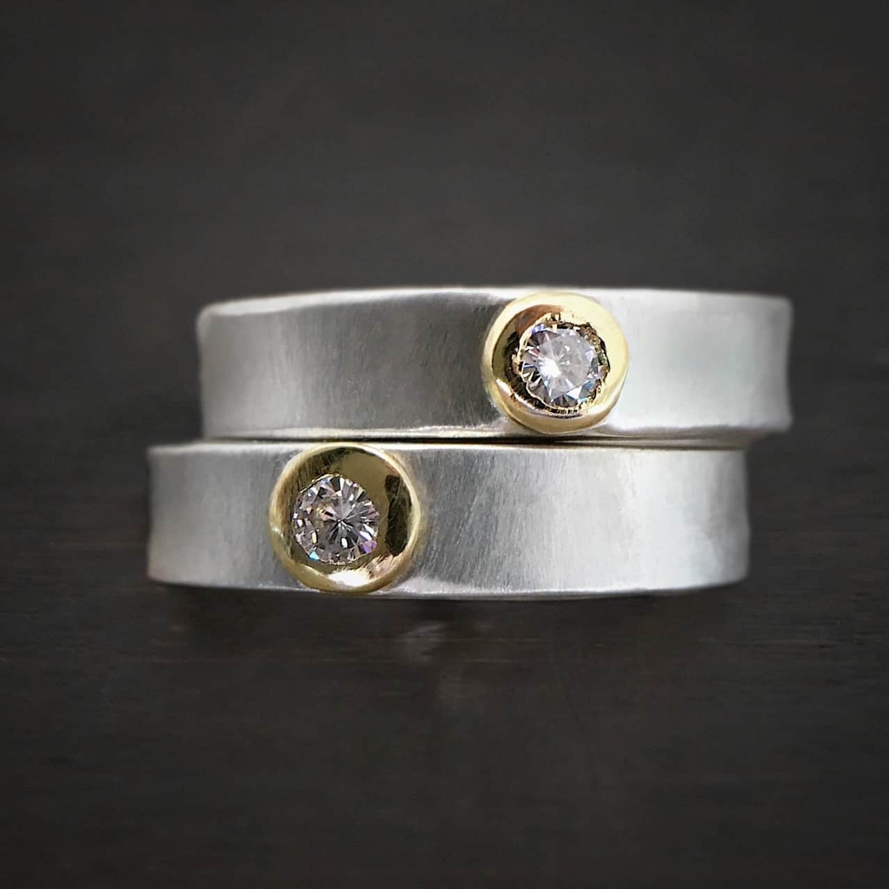 Photo of the "Adoration" Rings. Each ring has a small diamond in the center that is set in gold. Both rings are shiny.