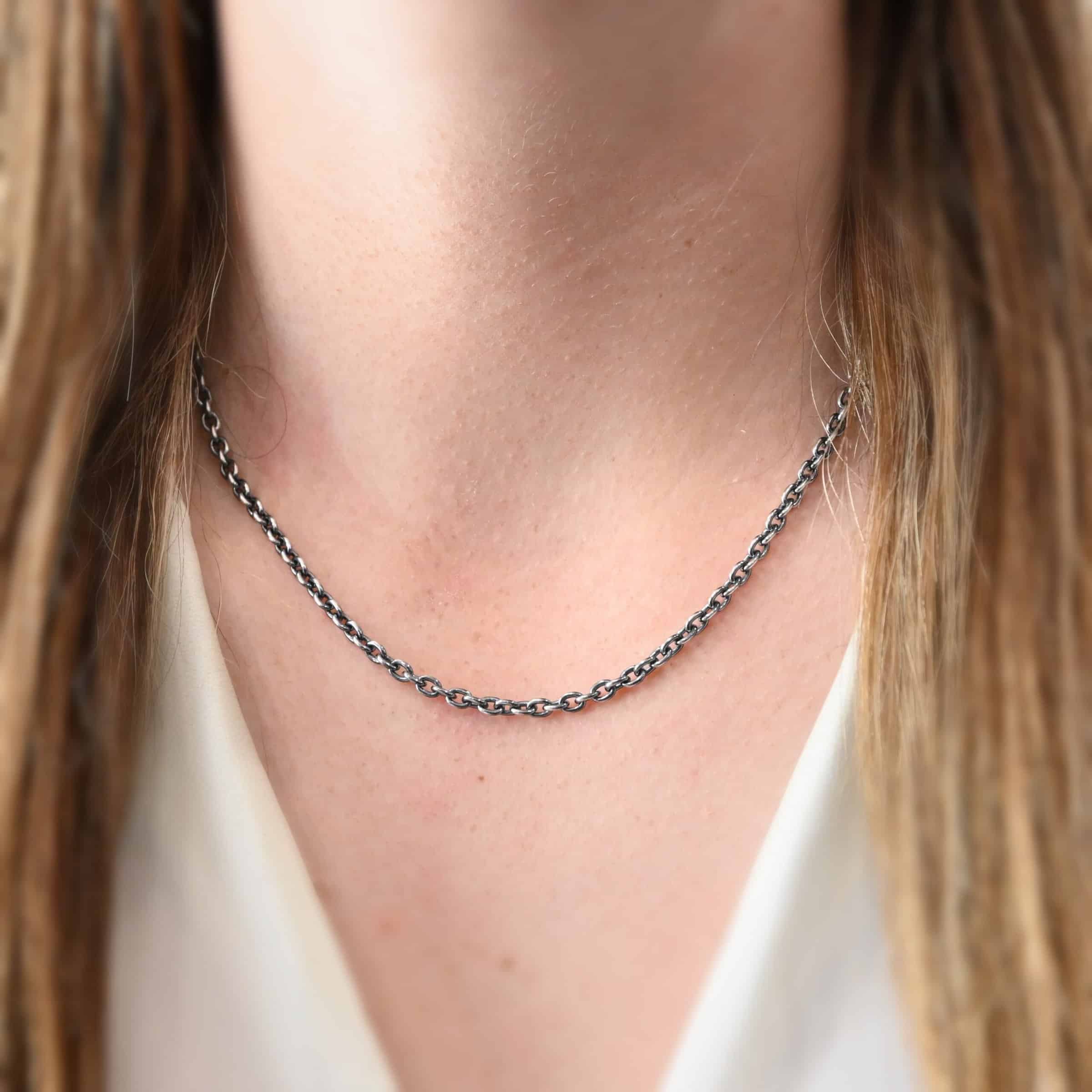 "Lauren" Chain as shown on a model. Model is wearing a white v-neck shirt. Lauren chain is 18 inches long on the model. It is oxidized sterling silver and it has links that are 5x4mmx1mm thick.