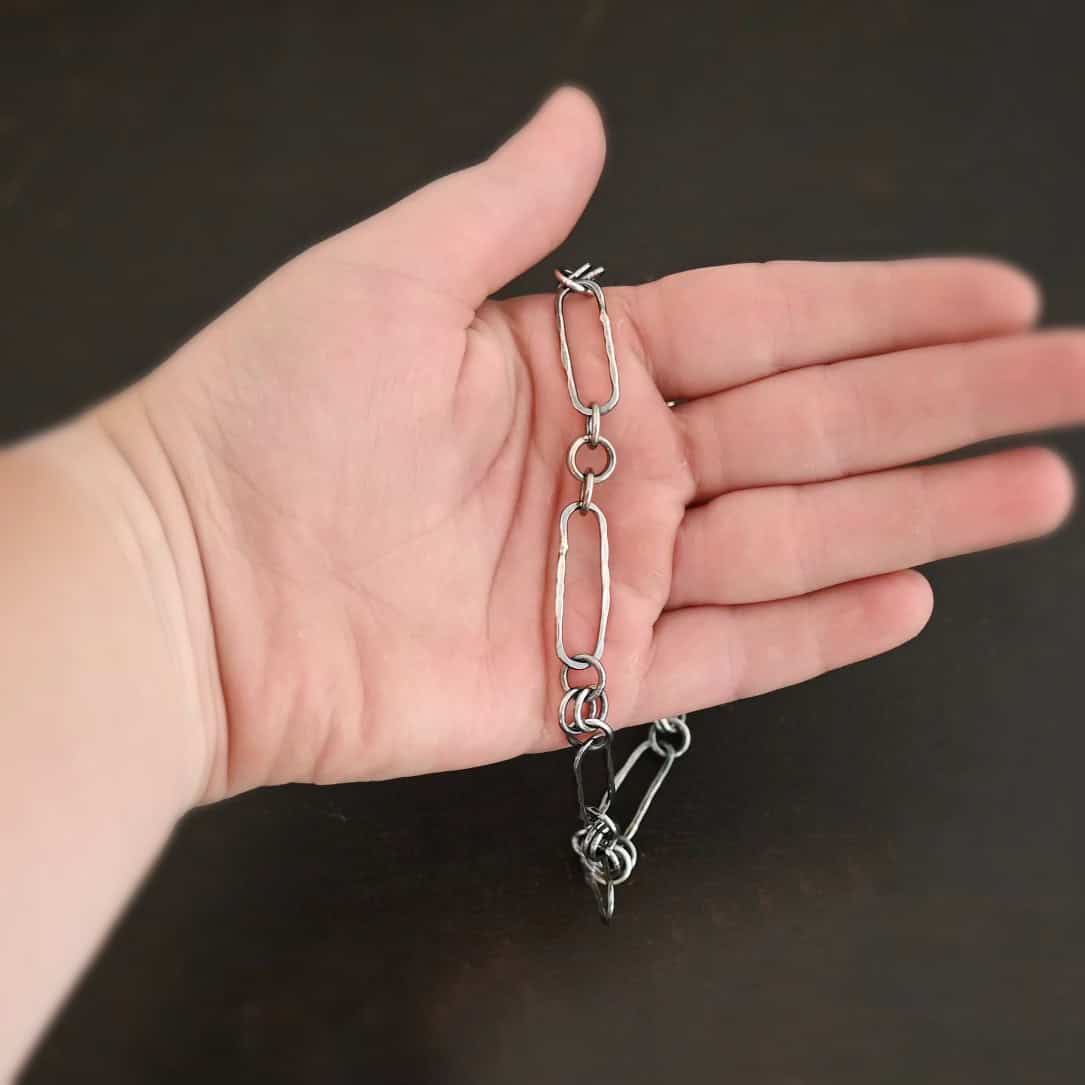 Close up of the "Bekah" Chain. This chain is handmade out of sterling silver and is oxidized. This chain has large oval links that are hammered and connected together by four jump rings. Chain is laying against a hand to demonstrate size of the links.