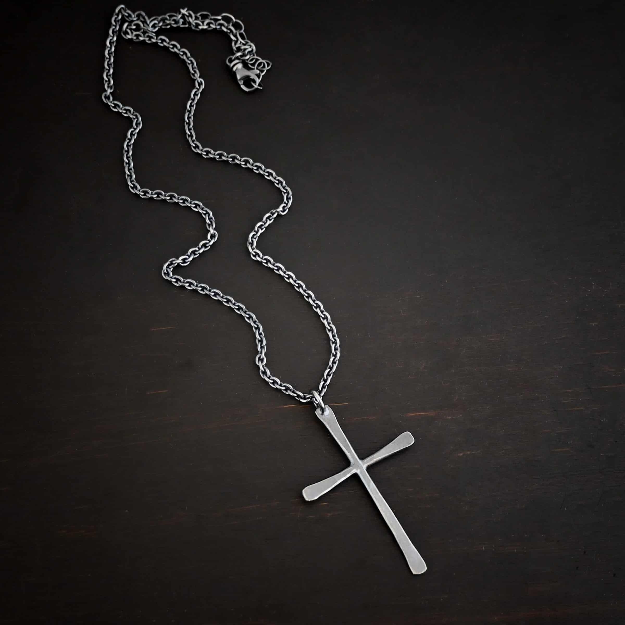 Ol Rugged Cross Necklace Photo of the "Ol' Rugged Cross" Necklace. Made out of sterling silver. There is a large cross that is hammered flat, but smooth. It is oxidized and has a loop soldered to the top of it. There is a chain that goes through the top of the necklace. Necklace is lying against a dark background.