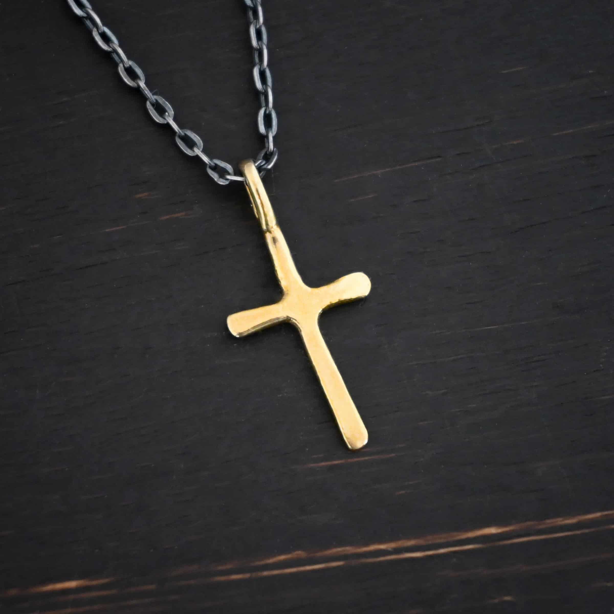 gold oxidized redeemer Photo of the "Redeemer" Necklace. Made out of 18k gold. Necklace has a very small cross that is hammered flat, but smooth, with a loop soldered to the top of it. The chain of the necklace is oxidized. Necklace is lying against a dark background.
