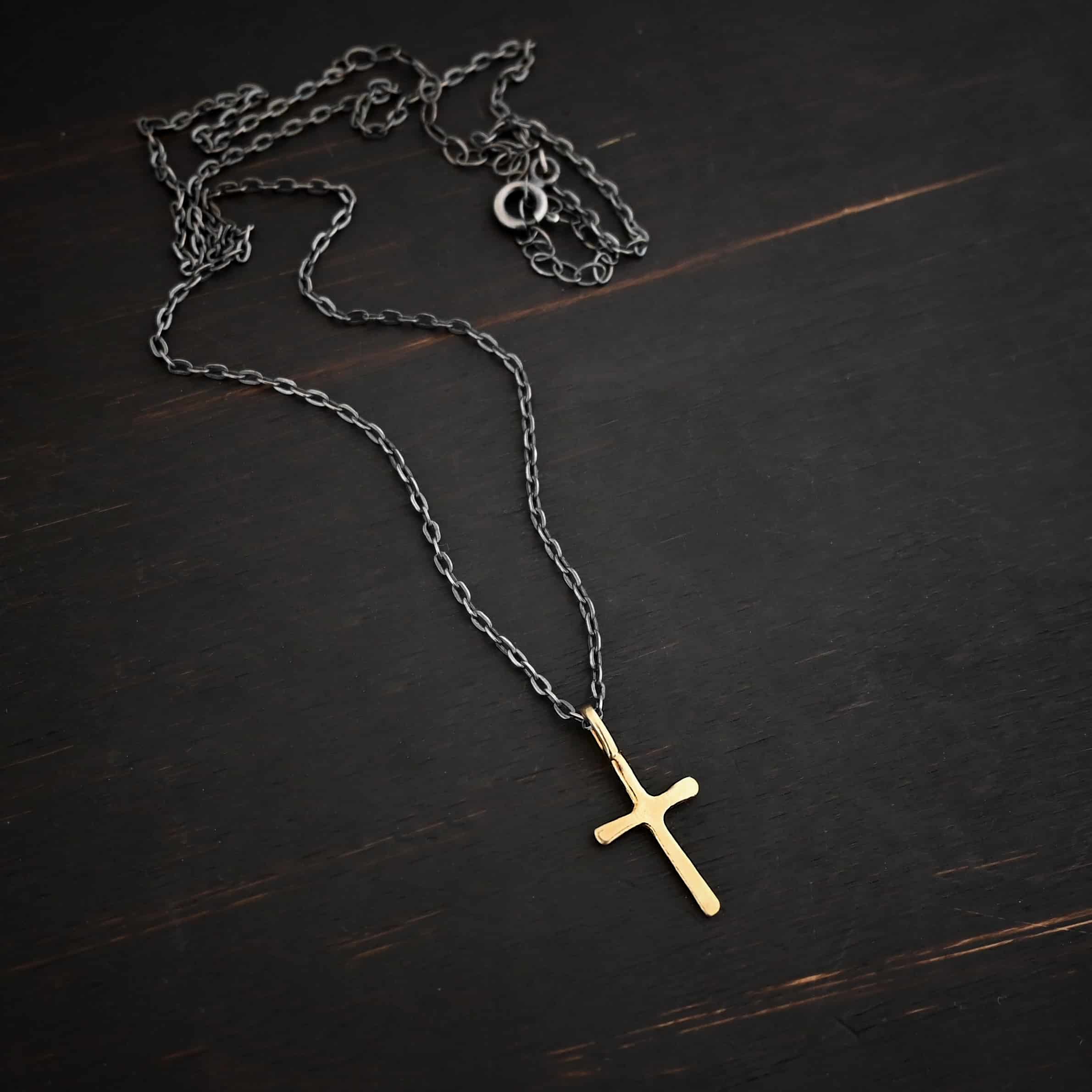 gold oxidized redeemer Photo of the "Redeemer" Necklace. Made out of 18k gold. Necklace has a very small cross that is hammered flat, but smooth, with a loop soldered to the top of it. The chain of the necklace is oxidized and has a spring ring clasp. Necklace is lying against a dark background.