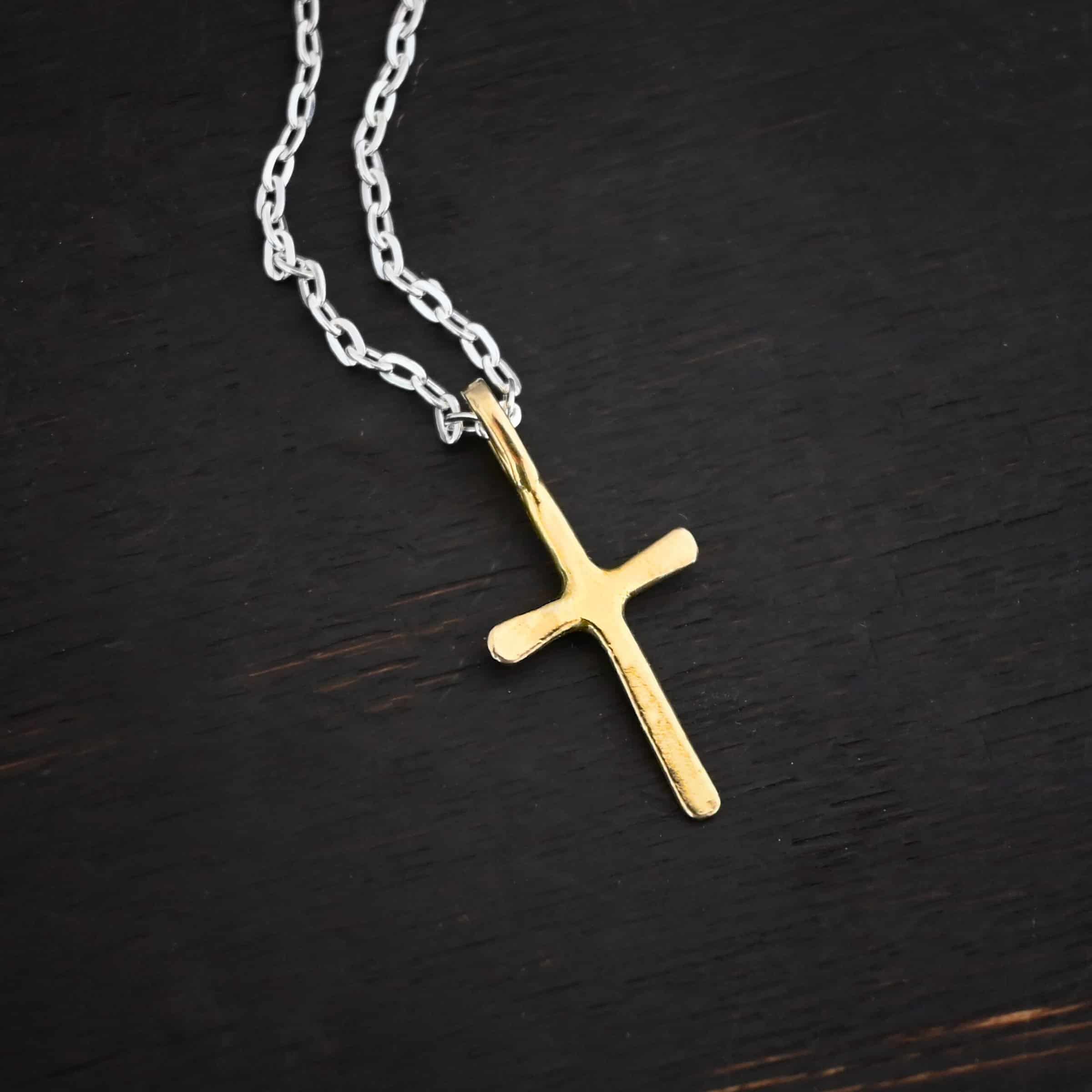 gold shiny redeemer Photo of the "Redeemer" Necklace. Made out of 18k gold. Necklace has a very small cross that is hammered flat, but smooth, with a loop soldered to the top of it. The chain of the necklace is shiny. Necklace is lying against a dark background.