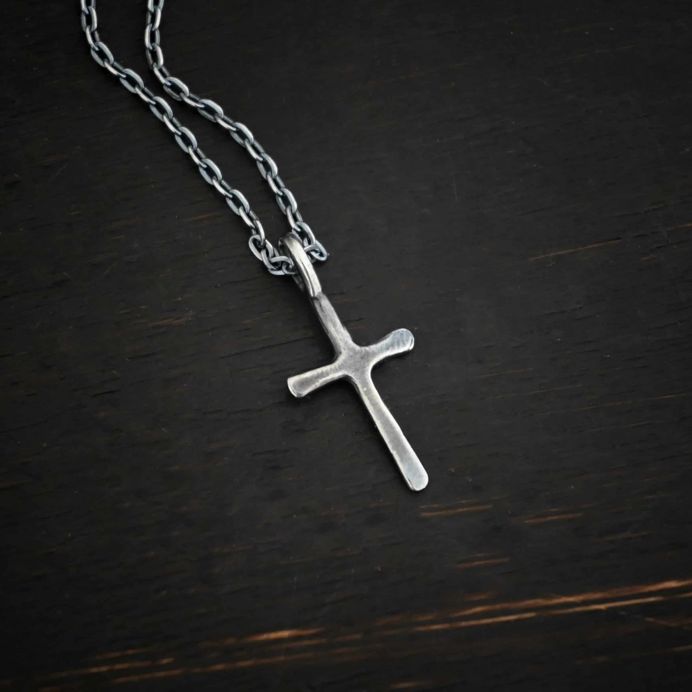 oxidized silver redeemer Photo of the "Redeemer" Necklace. Made out of sterling silver and oxidized. Necklace has a very small cross that is hammered flat, but smooth, with a loop soldered to the top of it. The chain of the necklace is oxidized. Necklace is lying against a dark background.