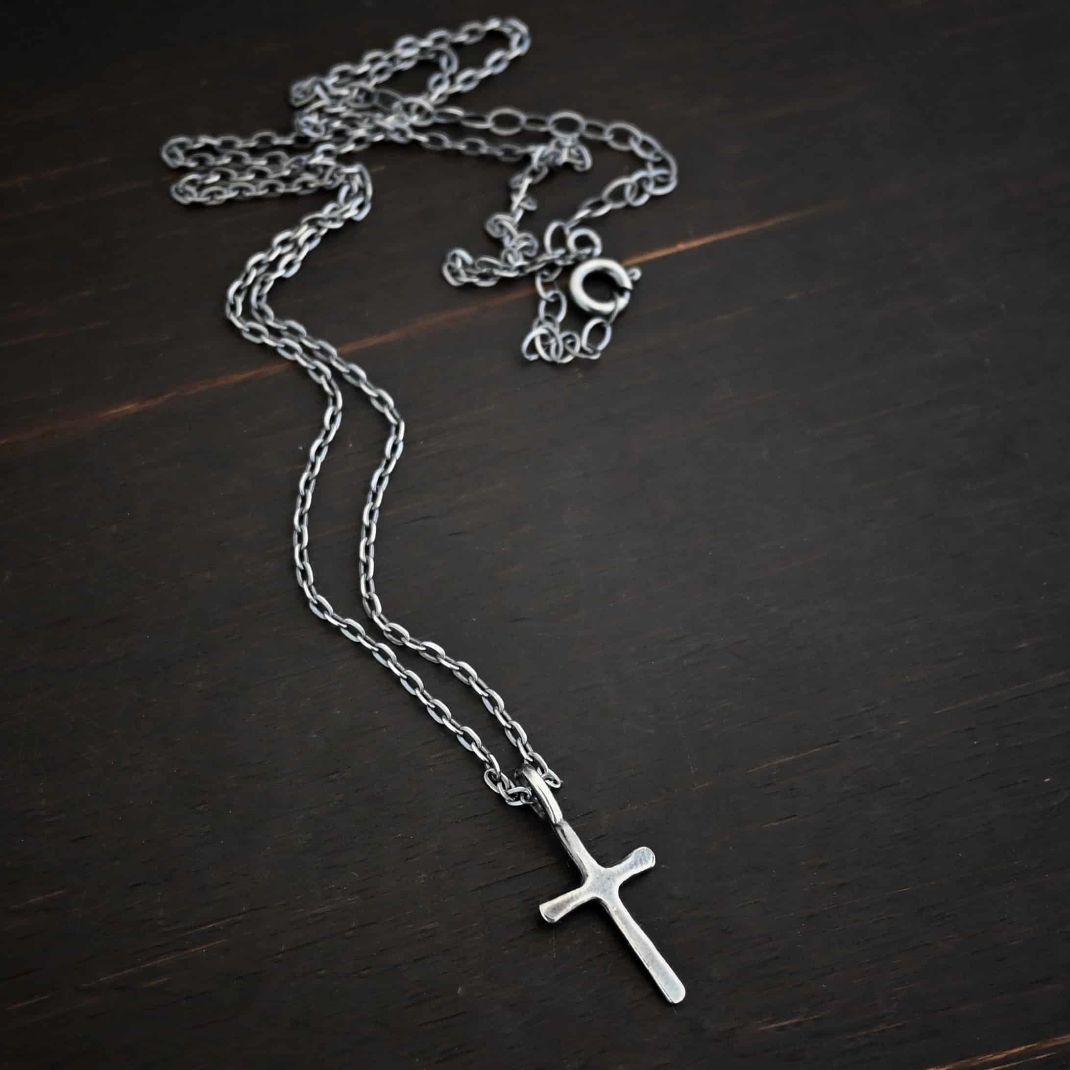 oxidized silver redeemer Photo of the "Redeemer" Necklace. Made out of sterling silver and oxidized. Necklace has a very small cross that is hammered flat, but smooth, with a loop soldered to the top of it. The chain of the necklace is oxidized and has a spring ring clasp. Necklace is lying against a dark background.