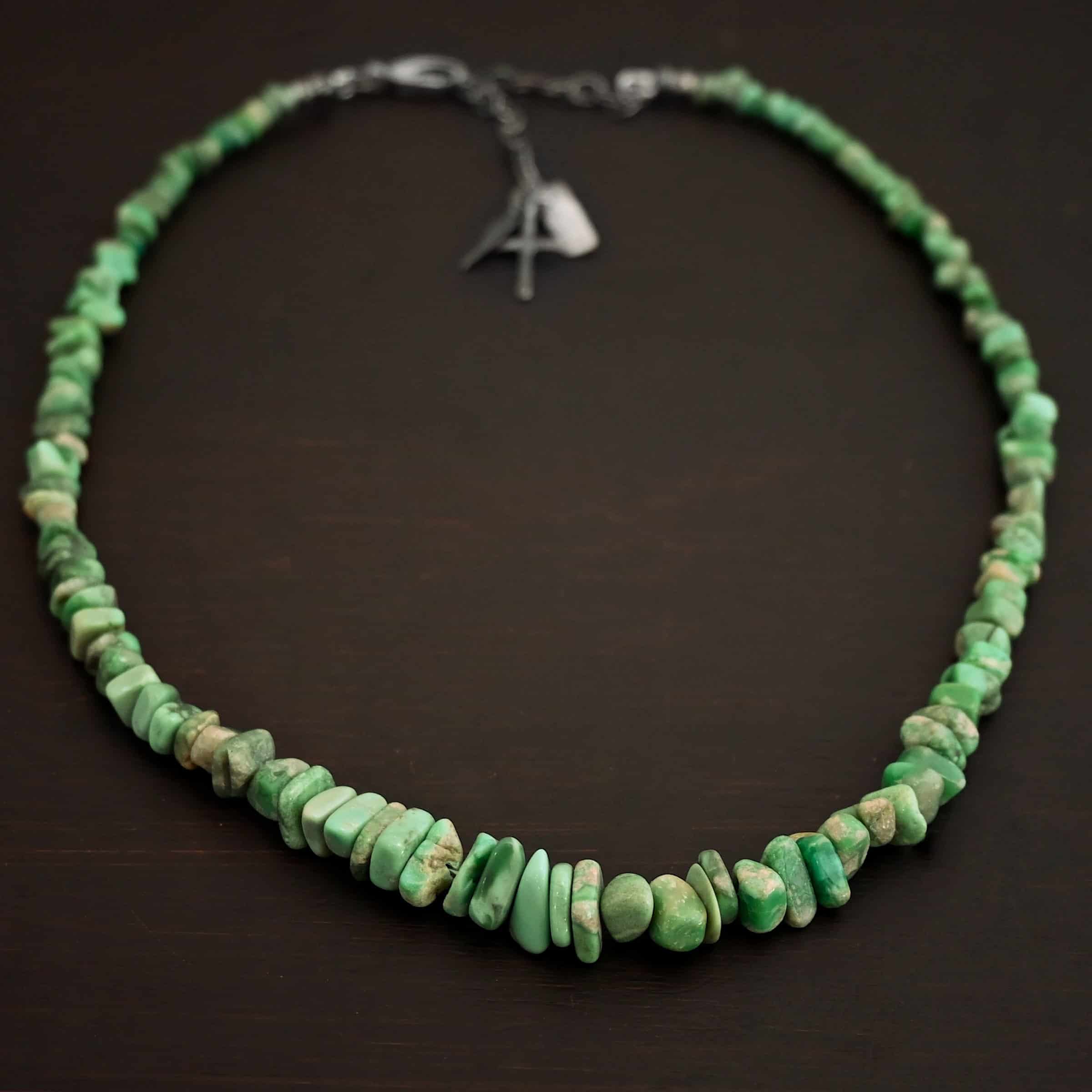 Photo of the "Rosalee" Necklace up close. Made out of sterling silver and variscite. Variscite beads that are different shapes and sizes are strung tight against one another for the entire necklace. The beads are a mix of mint green colors. Necklace is lying against a dark background.