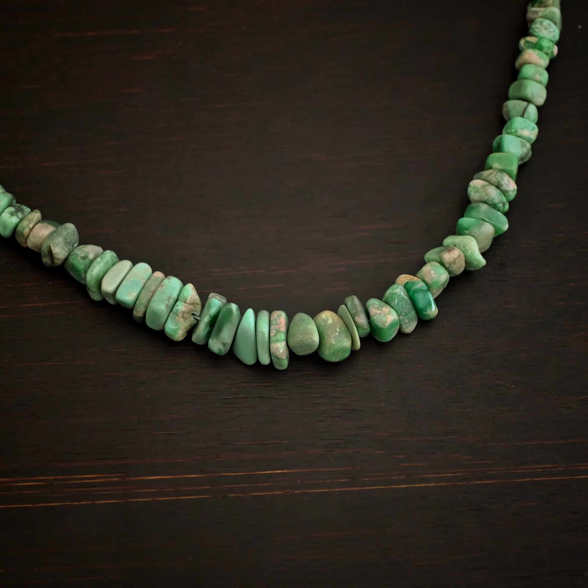 Photo of the "Rosalee" Necklace up close. Made out of sterling silver and variscite. Variscite beads that are different shapes and sizes are strung tight against one another for the entire necklace. The beads are a mix of mint green colors. Necklace is lying against a dark background.