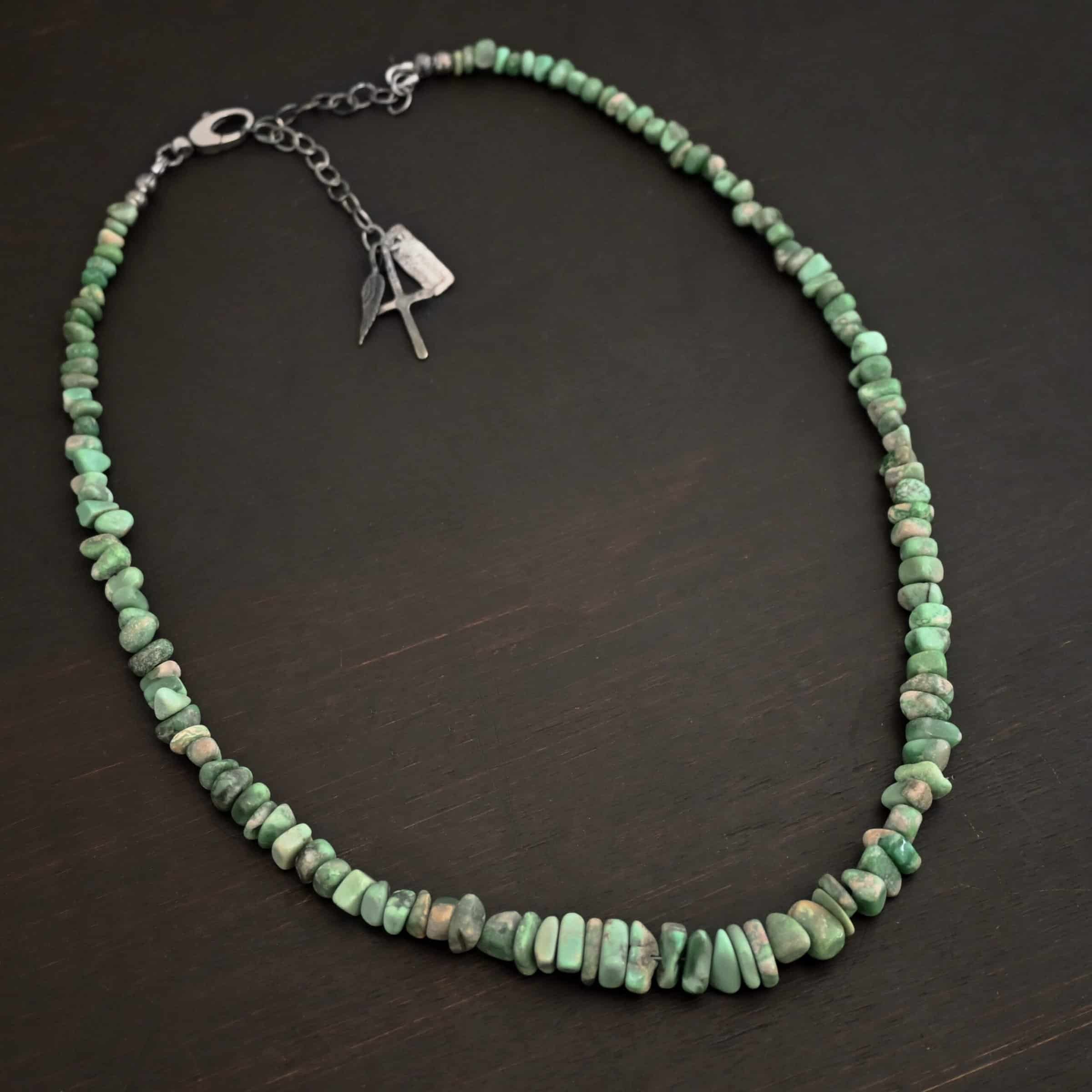 Photo of the "Rosalee" Necklace up close. Made out of sterling silver and variscite. Variscite beads that are different shapes and sizes are strung tight against one another for the entire necklace. The beads are a mix of mint green colors. Necklace is lying against a dark background.