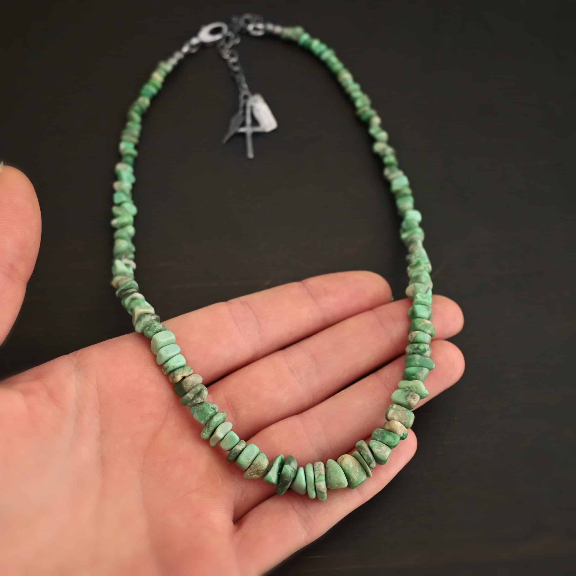 Photo of the "Rosalee" Necklace up close. Made out of sterling silver and variscite. Variscite beads that are different shapes and sizes are strung tight against one another for the entire necklace. The beads are a mix of mint green colors. Necklace is lying against the fingertips of a hand.