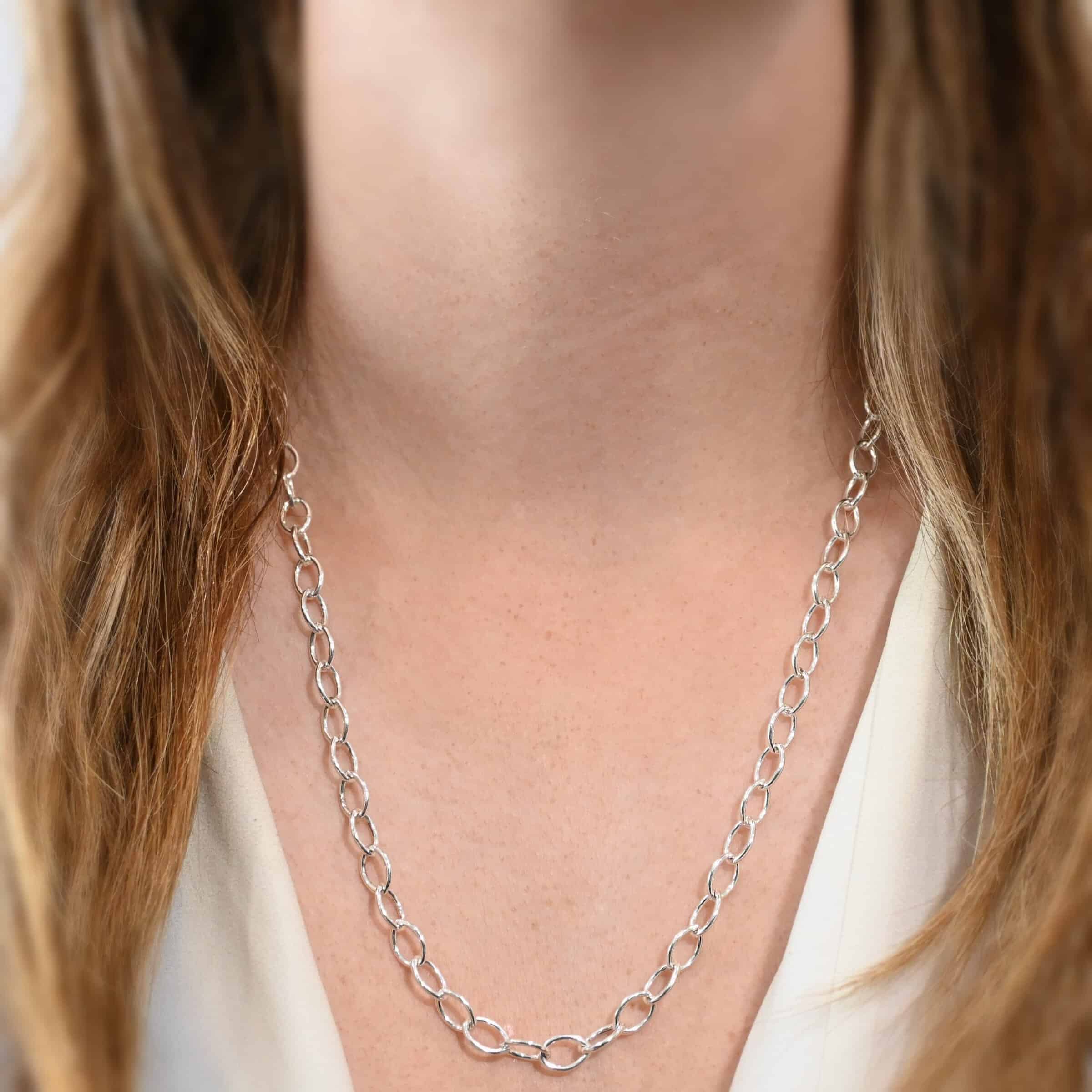 Sky Chain, shiny, hammered, 24" The "Sky" Chain as shown on a model. Made out of sterling silver, shiny, and hammered. It is 24 inches long. Shown on a model wearing a white v-neck shirt.