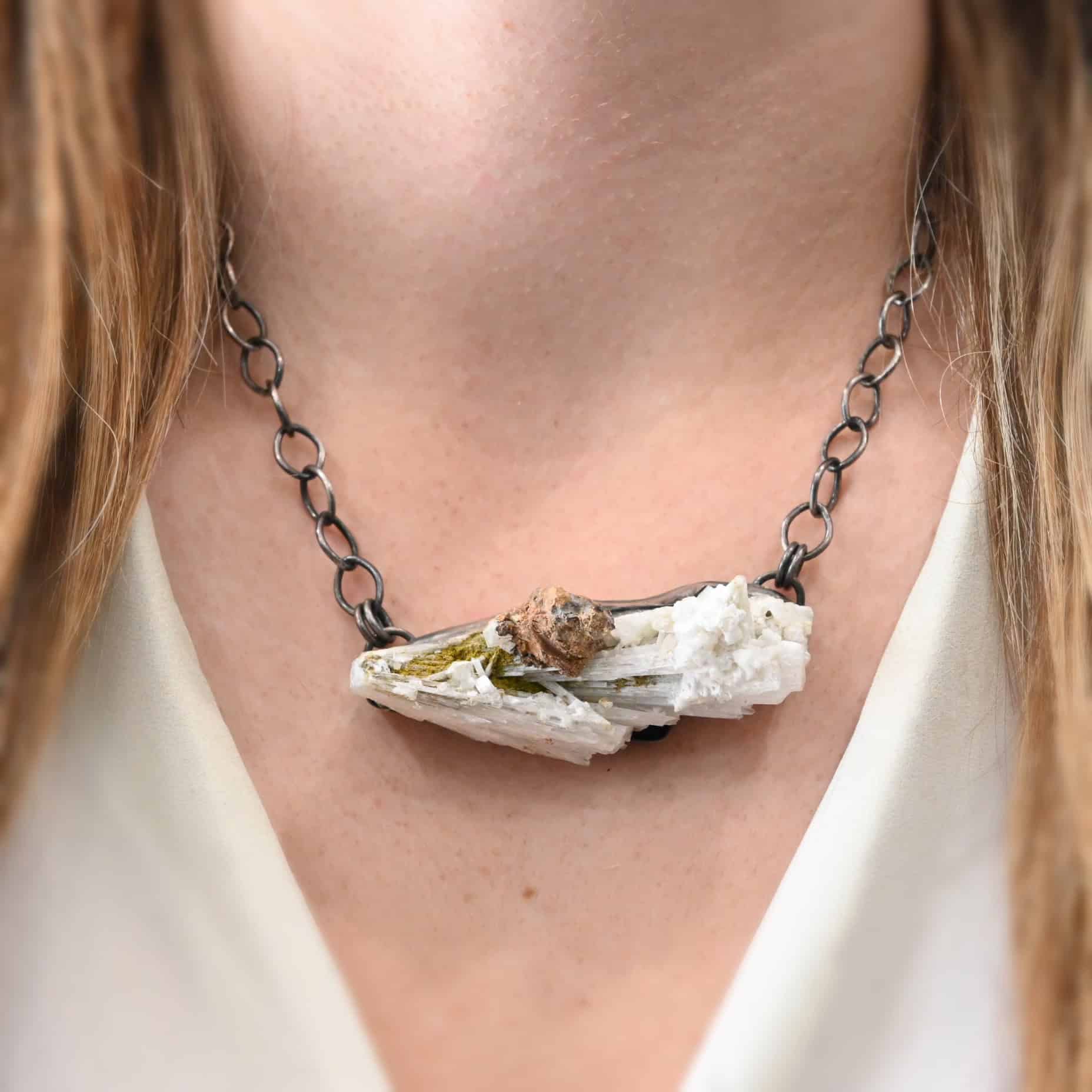 Driftwood Necklace The "Driftwood" Necklace as shown on a model. Necklace is made out of sterling silver and calcitite. Pendant measures 1x3." Comes on a sterling silver "Sky" chain that is oxidized with large circle links. Model is wearing a white v-neck.