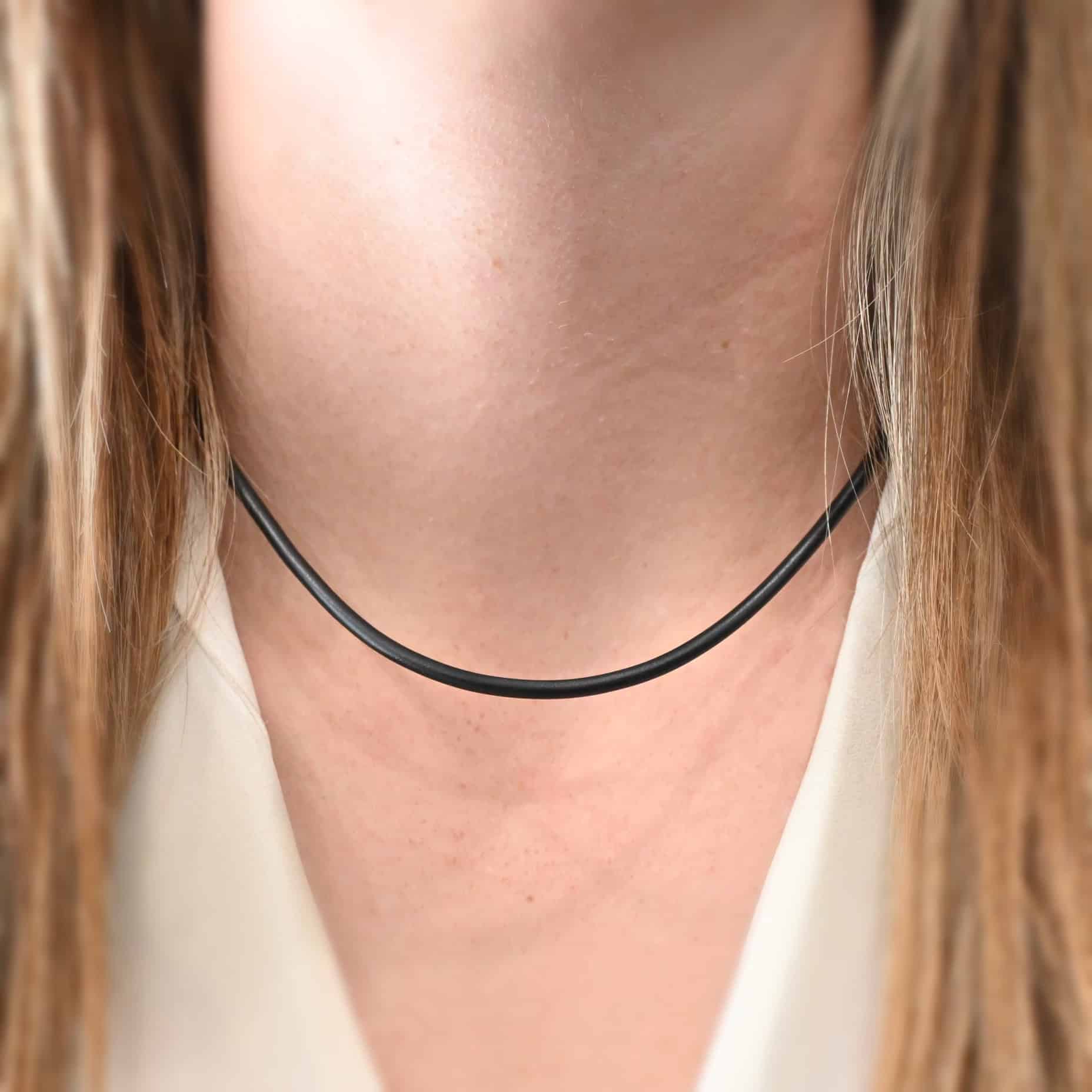 "Wren Wire" Chain as shown on a model. This is a black leather chain that is shown on a model at 18 inches long. Model is wearing a white v-neck shirt.