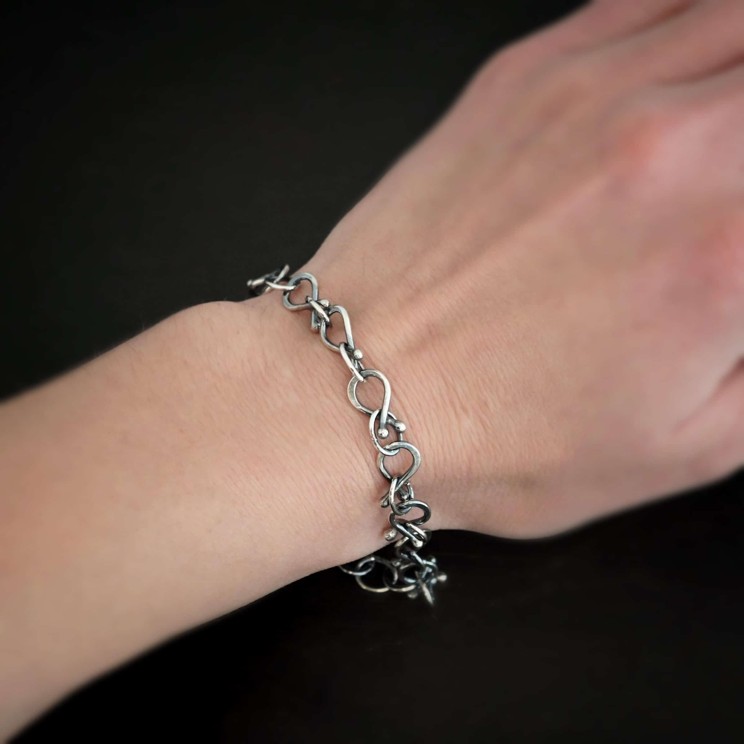 Loretta Bracelet Photo of the "Loretta" Bracelet. Made out of sterling silver. The bracelet is made out of pear shaped. The top of each link has two silver balls, one for each end at the top. Between each teardrop link is a circle link of silver. There is a cross and angel wing charm on the bracelet, and bracelet has a lobster claw clasp. Bracelet is worn by a model to demonstrate size.