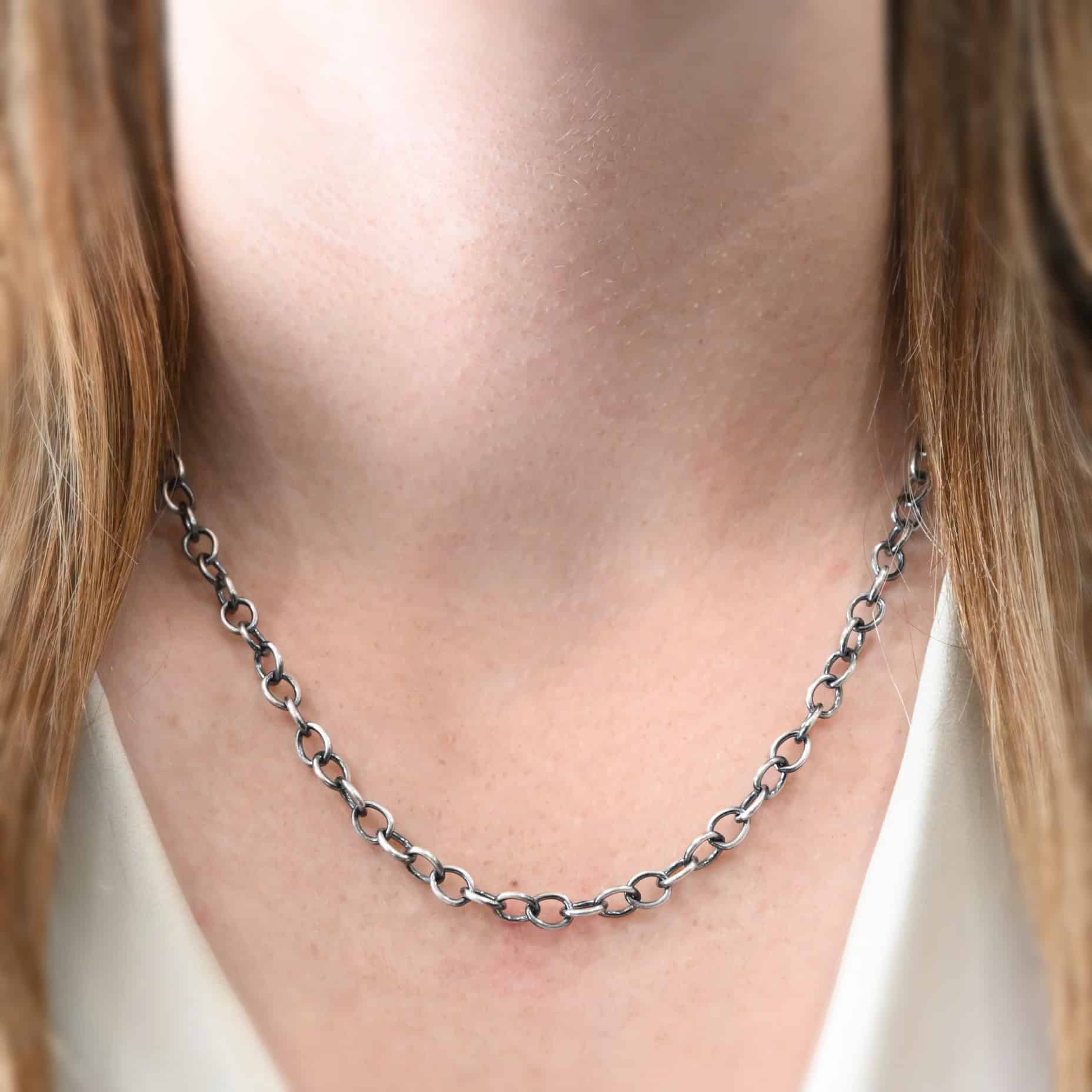 Jay Chain Oxidized "Jay" Chain as shown on a model. This chain is made out of sterling silver, and is shown at twenty inches long and oxidized. Heavy oval links measure 7.2×5.7mm. Model is wearing a white v-neck shirt.