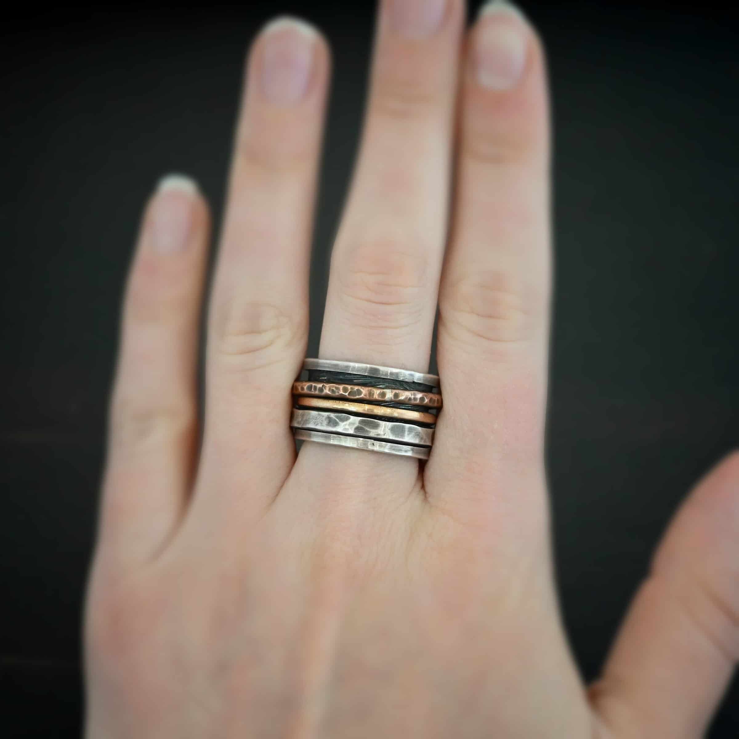 Royal Revolver Ring Photo of the "Royal Revolver" Ring. Made out of sterling silver, copper, and 14k gold. The top and bottom of the ring are silver, and there is a gap in the center of the ring. The gap is taken up by a hammered copper spinner, a smooth 14k gold spinner, and a thick, hammered sterling silver spinner. Each band in the center spins around. Ring is worn by a model to demonstrate size.