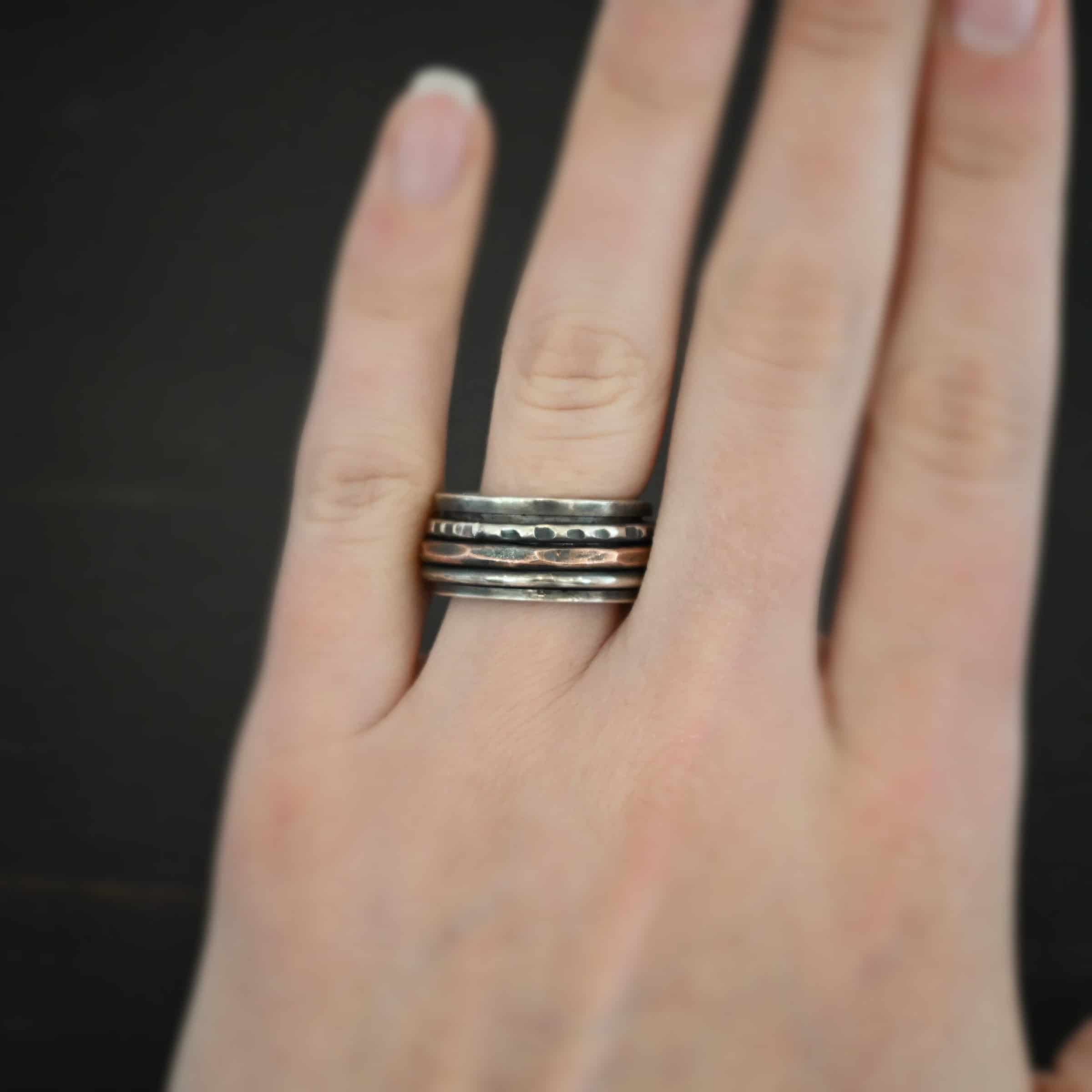 Revolver Ring Photo of the "Revolver" Ring. Made out of sterling silver and copper. The top and bottom of the ring are silver, and there is a gap in the center of the ring. The gap is taken up by a hammered copper spinner and a thick, hammered sterling silver spinner, as well as a smooth sterling silver spinner. Each band in the center spins around. Ring is worn by a model to demonstrate size.