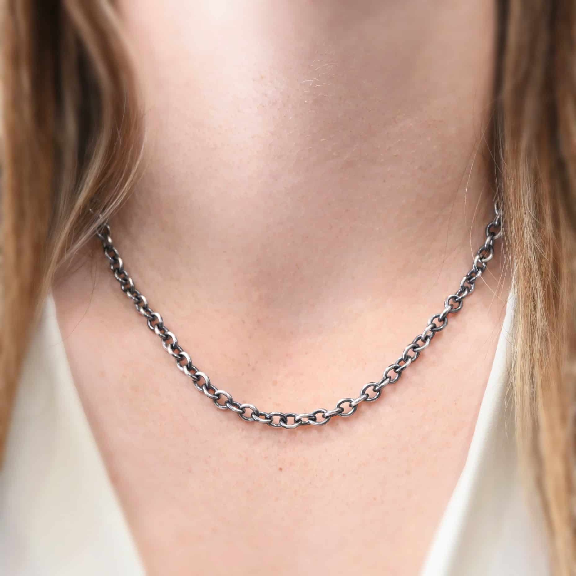 "Joy" Chain as shown on a model. This chain is made out of sterling silver. Shown on model as oxidized and eighteen inches long. Model is wearing a white v-neck shirt. Links measure 6.5×5.4mm.