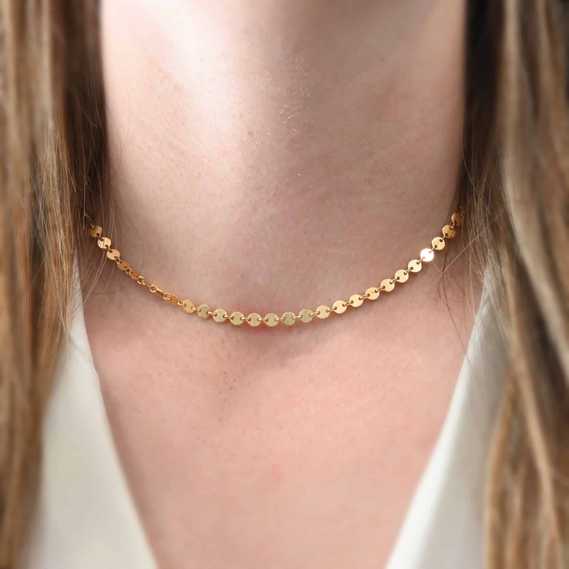 "Gypsy Coin" Chain as shown on a model. Chain is gold filled and shown worn at fifteen inches long on a model wearing a white v-neck shirt.