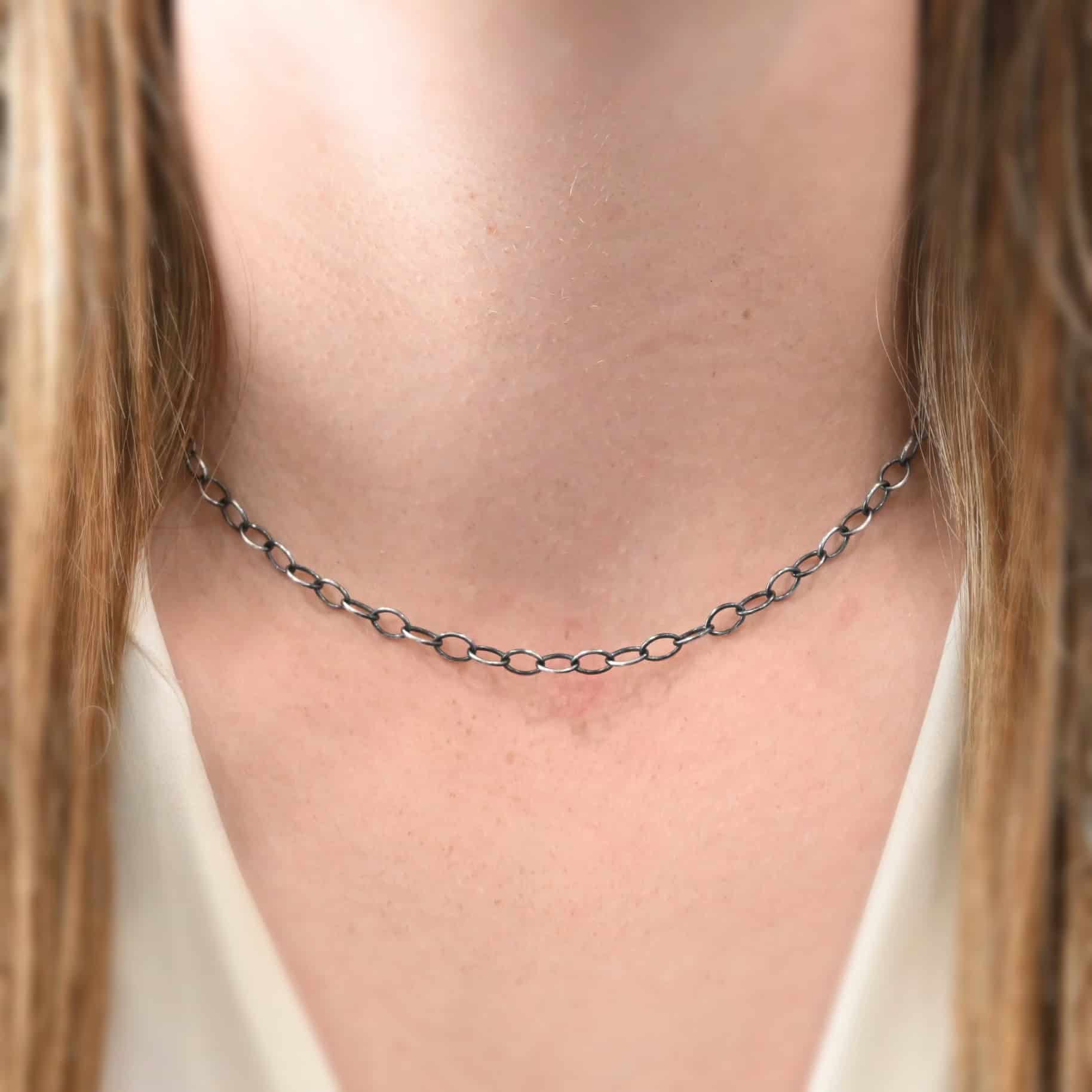 Willow Chain "Willow" Chain as shown on a model. Chain is shown as oxidized and at sixteen inches long. Model is wearing a white v-neck shirt. Oval links of the chain measure 6.5mmx7mm.