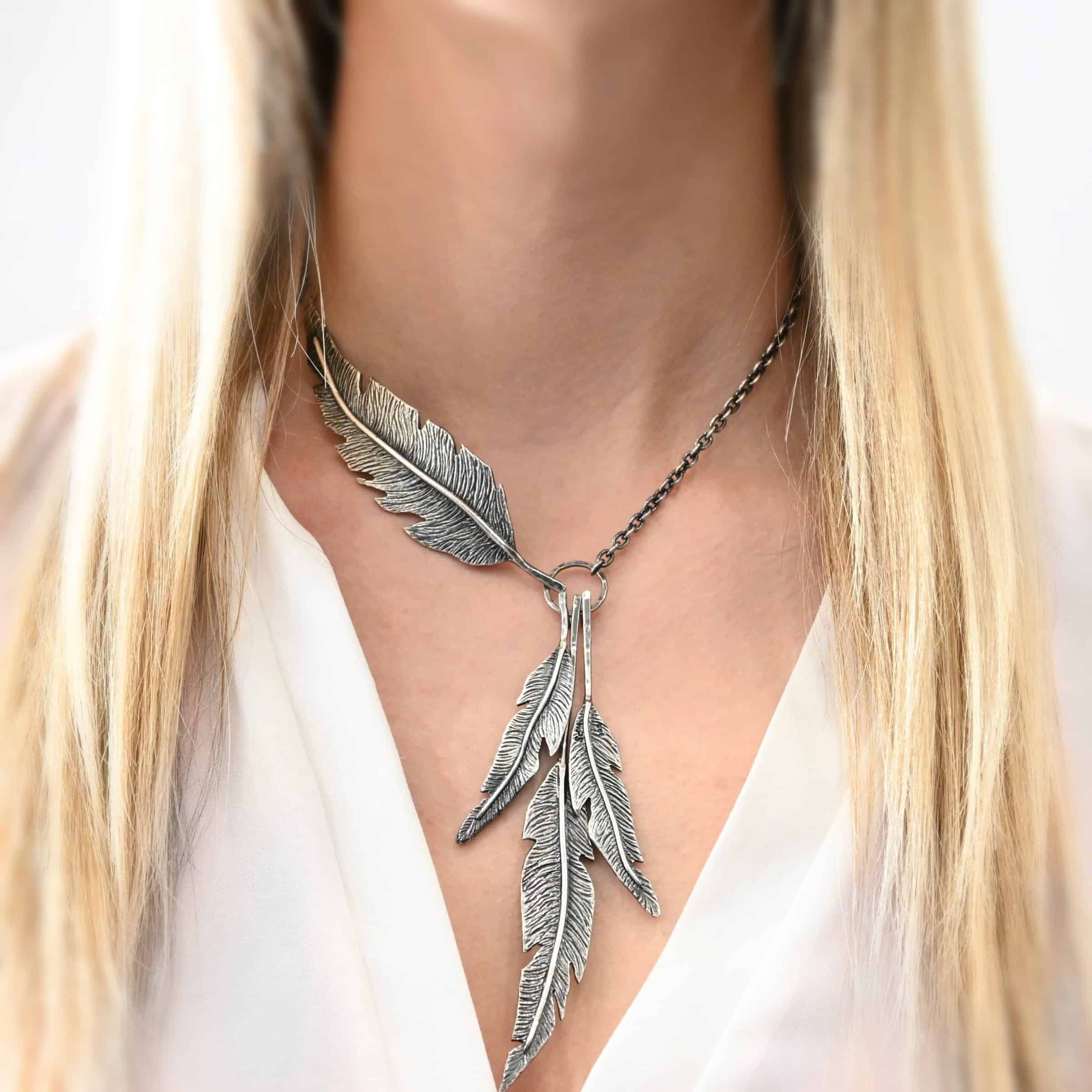 Photo of the "Freedom" Necklace. There are three, large, sterling silver feathers that hang from a loop. There is another feather that is attached to the loop closer to the top, and it is attached horizontally to the left side of the chain, so it doesn't hang down. Necklace is worn by a model.