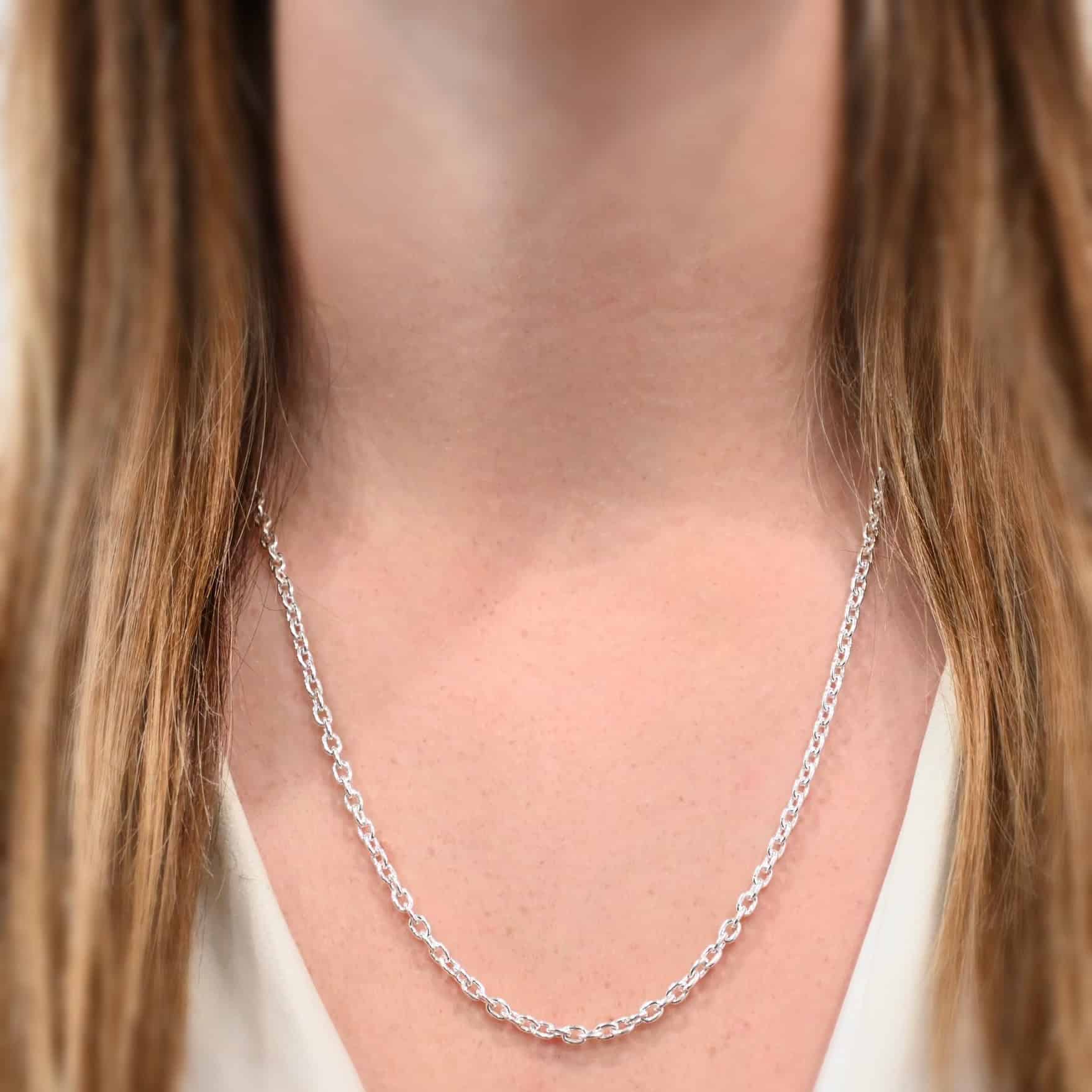 "Lauren" Chain as shown on a model. Model is wearing a white, v-neck shirt. Lauren chain is 24 inches long on the model. It is shiny sterling silver and it has links that are 5x4mmx1mm thick.