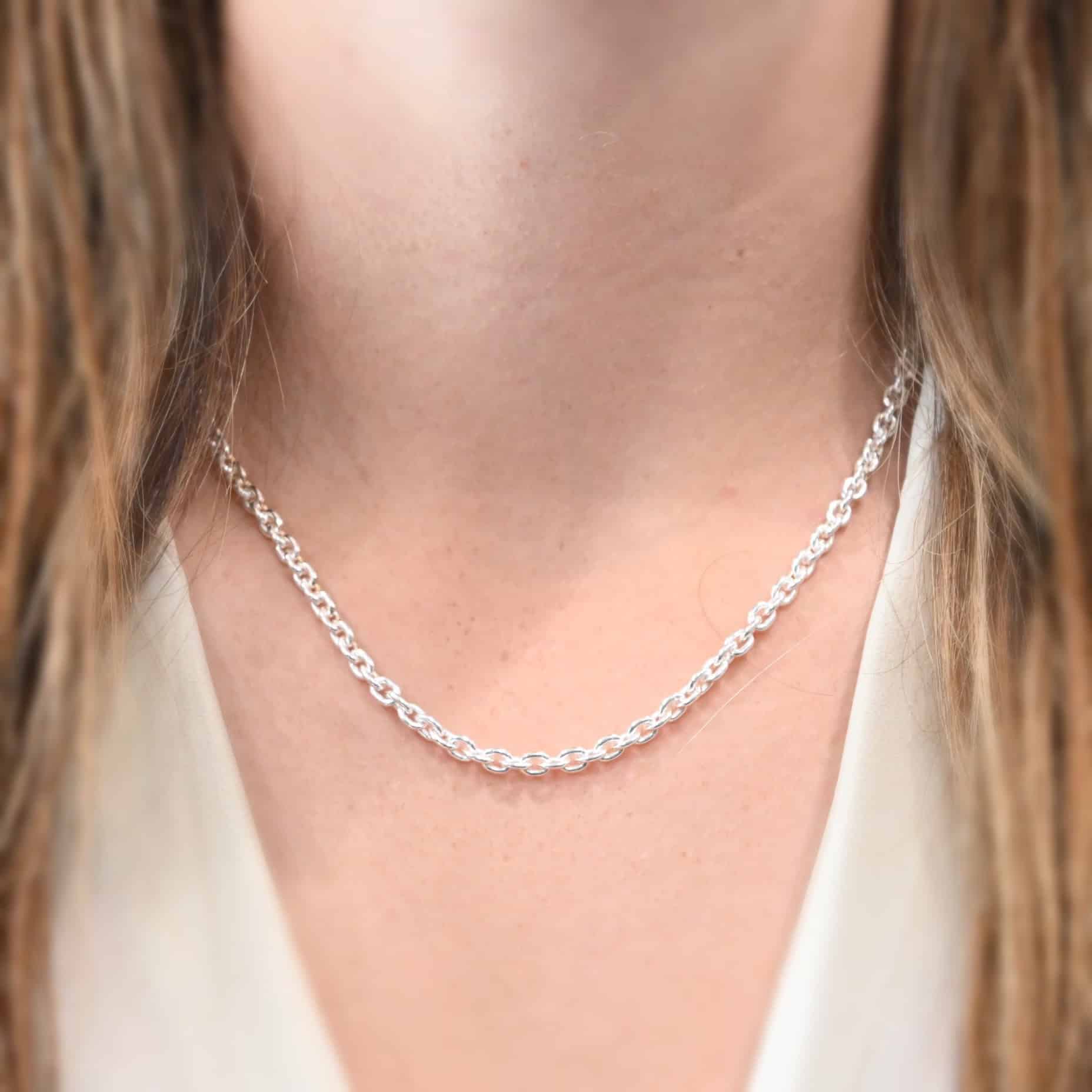 Joan Chain, eighteen inches long, shiny "Joan" Chain as shown on a model. Chain is sterling silver and eighteen inches long and shiny. Model is wearing a white V-neck shirt.