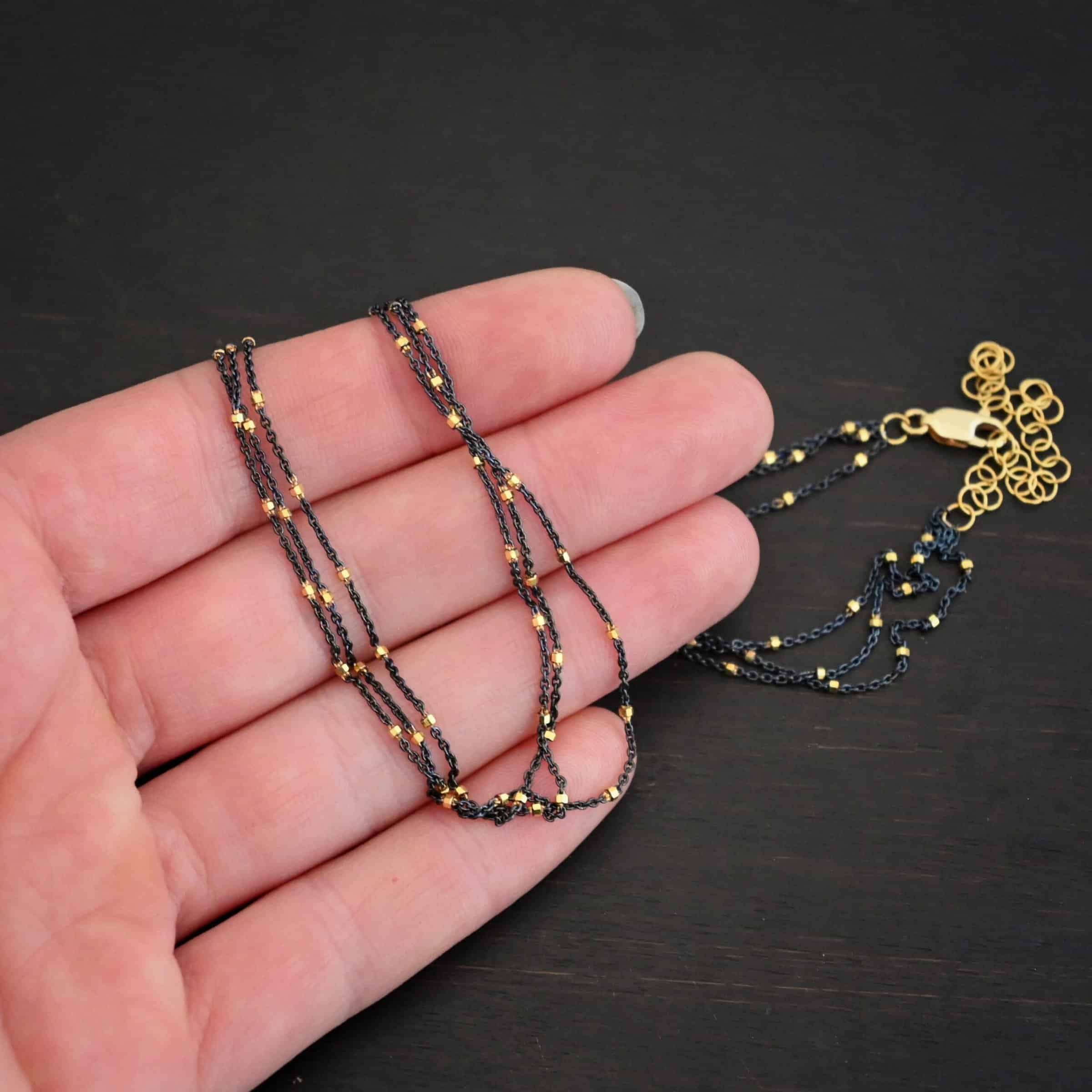 Night in Paris Chain "Night In Paris" Chain as shown up close. Sterling Silver & 14k yellow gold filled beads that are 1.5mm thick. The chain is 1.2mm thick. The chain is made out of three separate strands that meet at the back to make one chain. Chain is lying against the fingertips of a hand to demonstrate thickness.