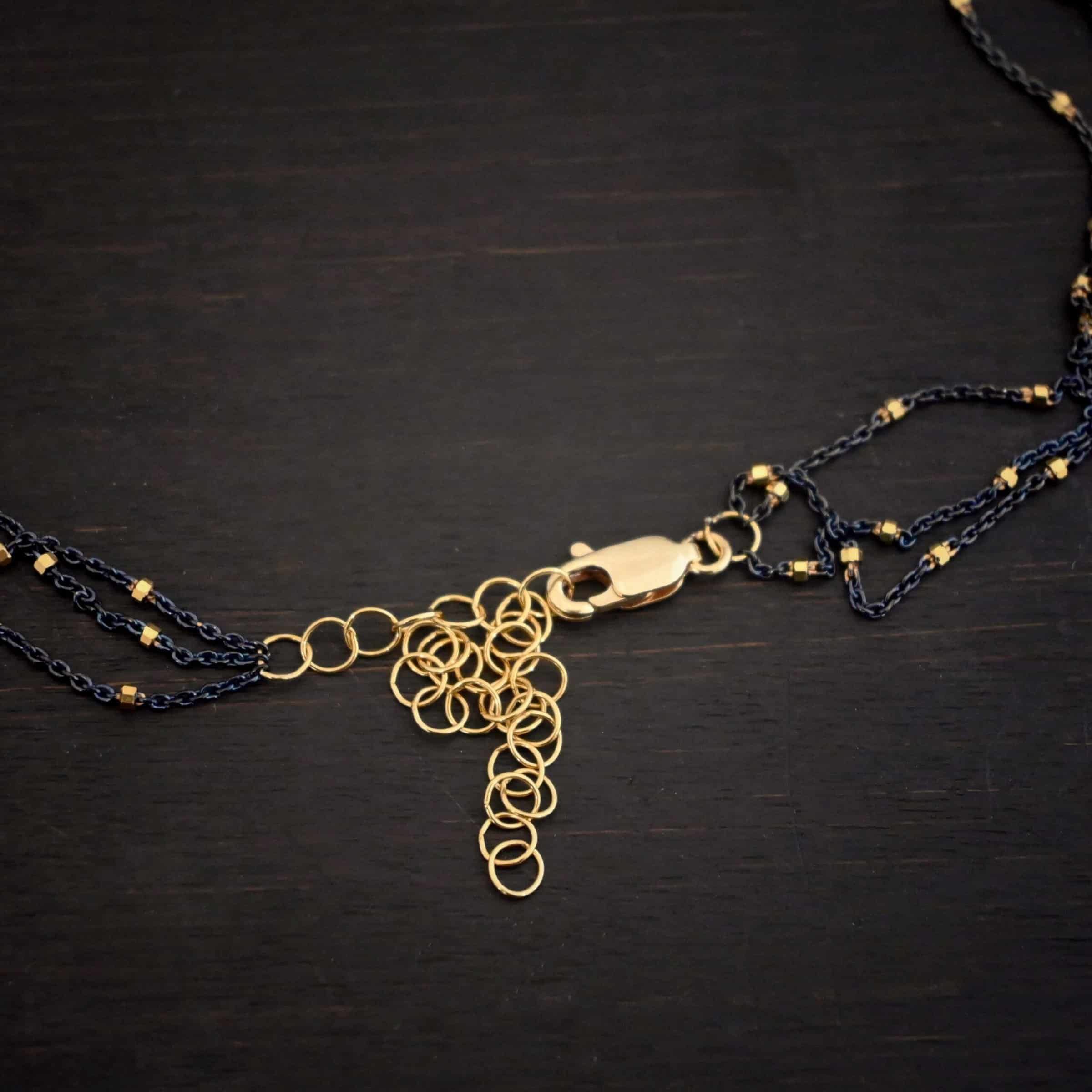 Night in Paris chain "Night In Paris" Chain as shown up close. Sterling Silver & 14k yellow gold filled beads that are 1.5mm thick. The chain is 1.2mm thick. The chain is made out of three separate strands that meet at the back to make one chain. Chain has a gold filled lobster claw clasp with a gold filled chain extension. Necklace is lying agains a dark background.