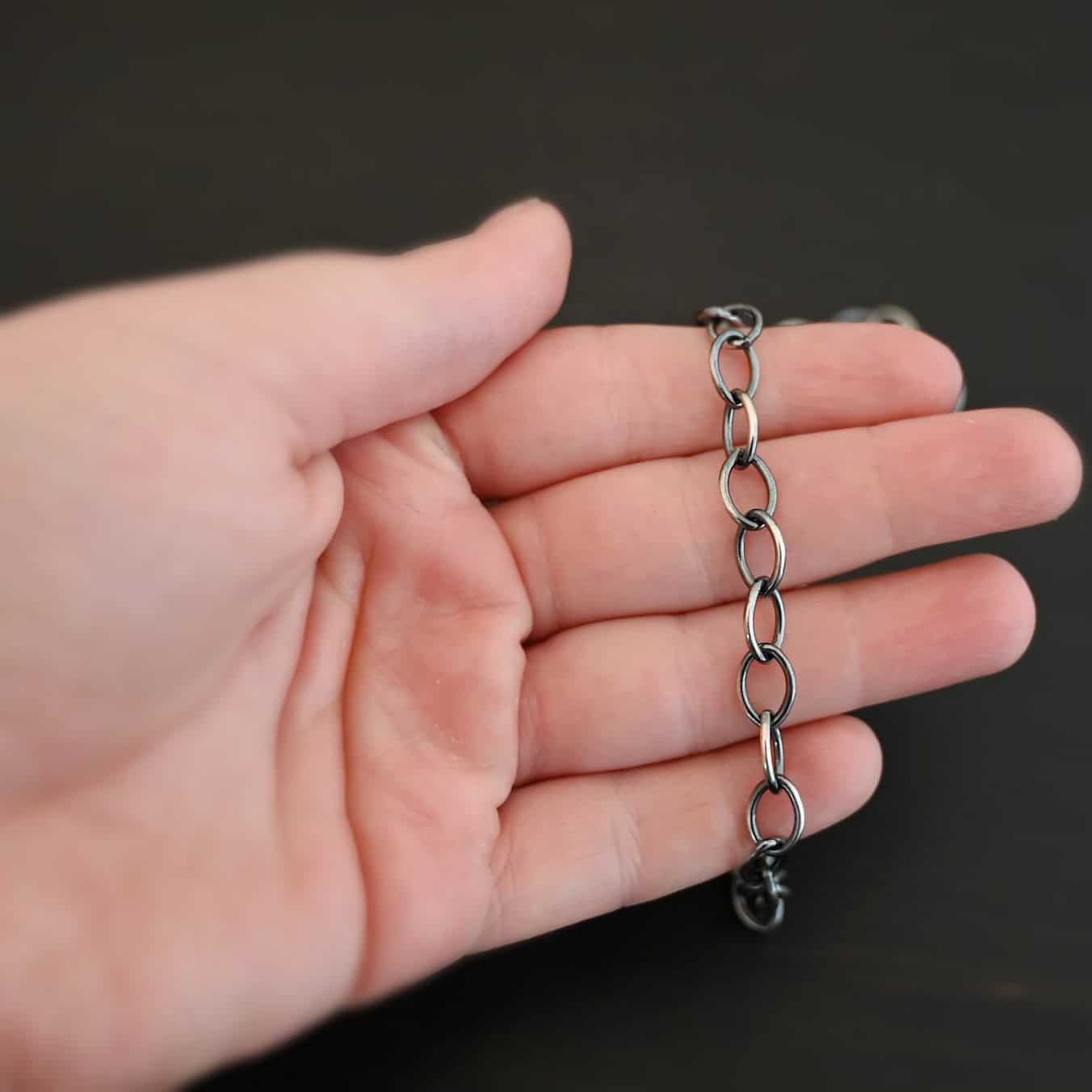 Sky Chain, Oxidized, Smooth Oxidized sterling silver Sky Chain that is made with large oval links that are smooth and are all connected together laying on a hand that is resting against a dark background