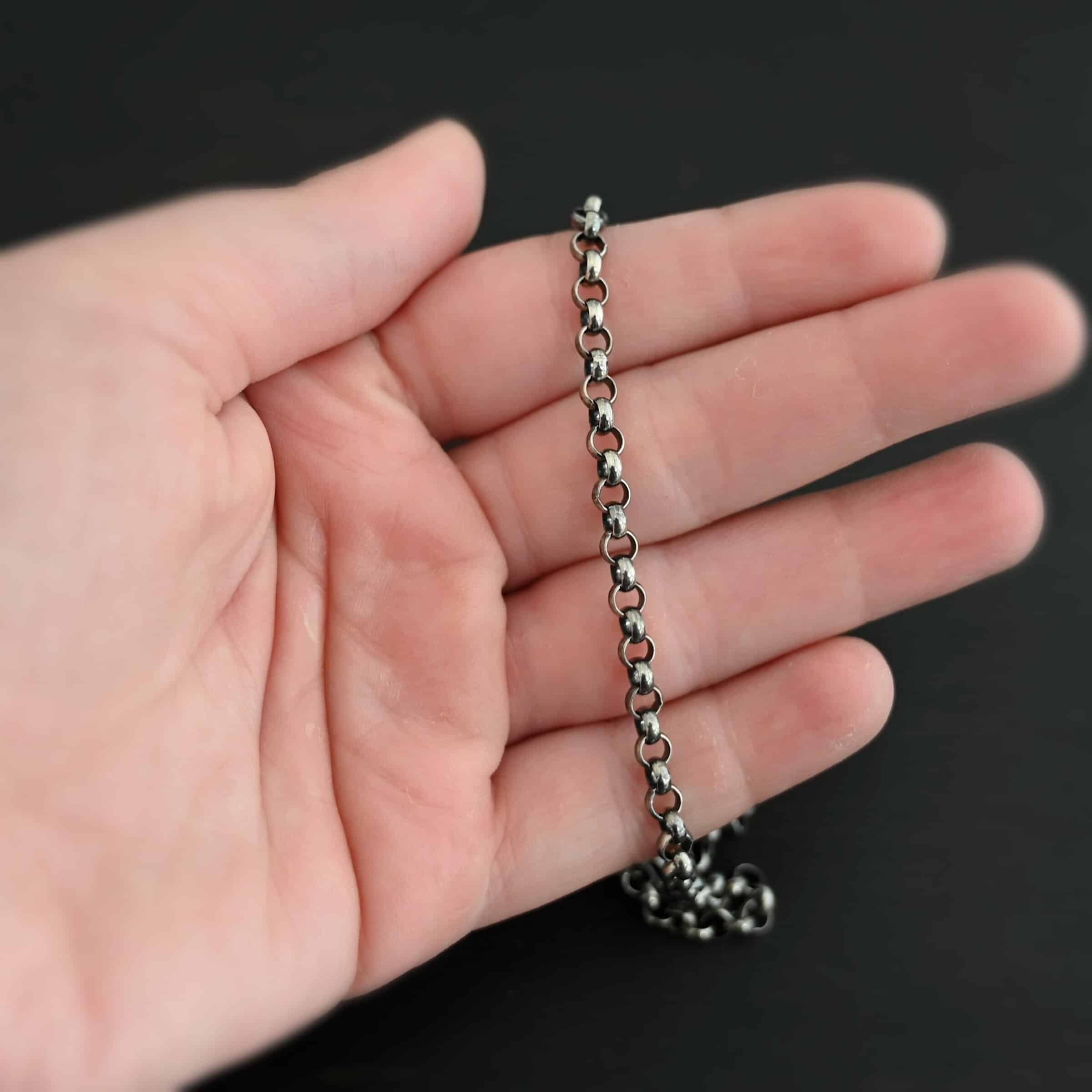 Oxidized sterling silver Roxy Rolo Chain that is made with small circular links all connected together laying on a hand that is resting against a dark background