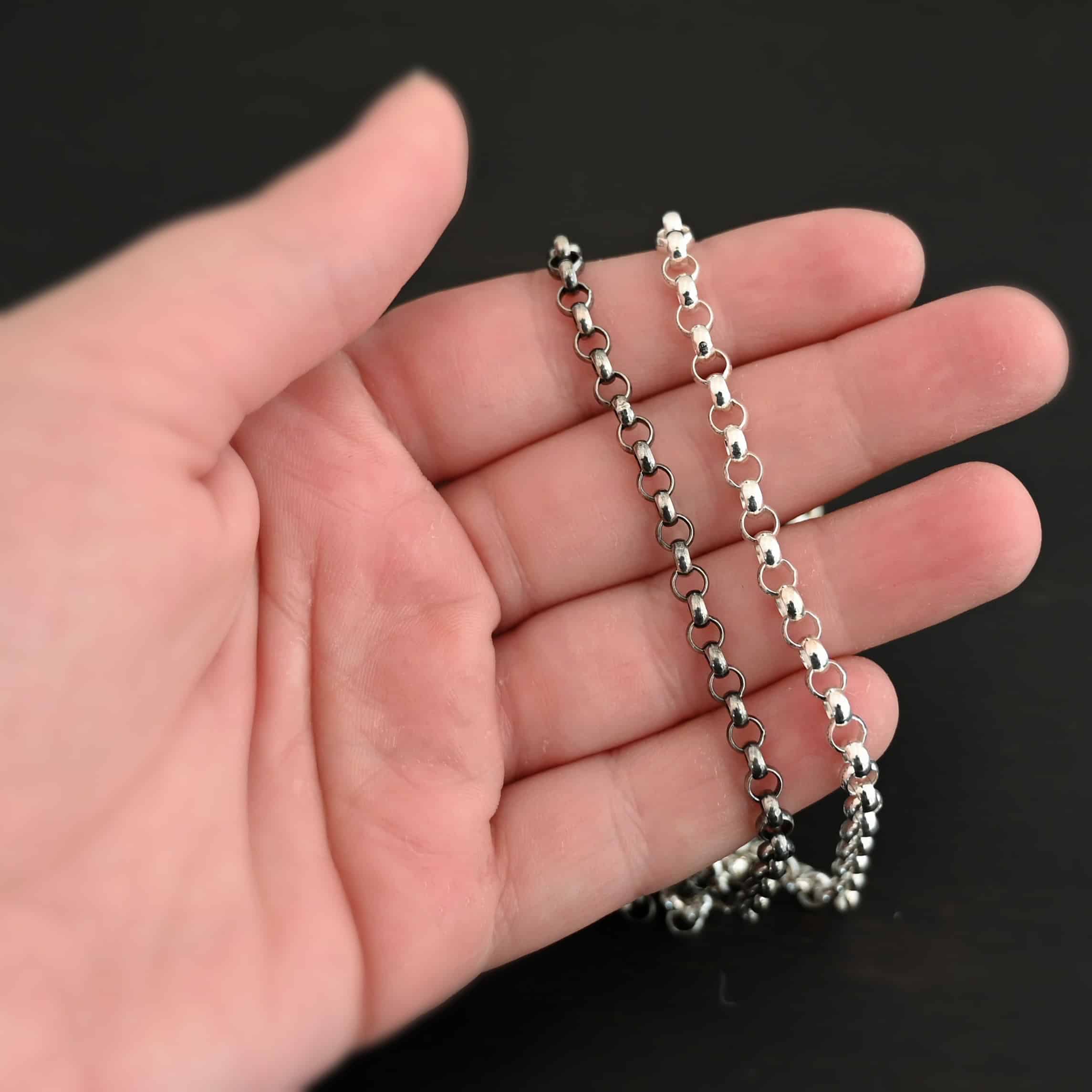 Shiny & Oxidized sterling silver Roxy Rolo Chain that is made with small circular links all connected together laying on a hand that is resting against a dark background