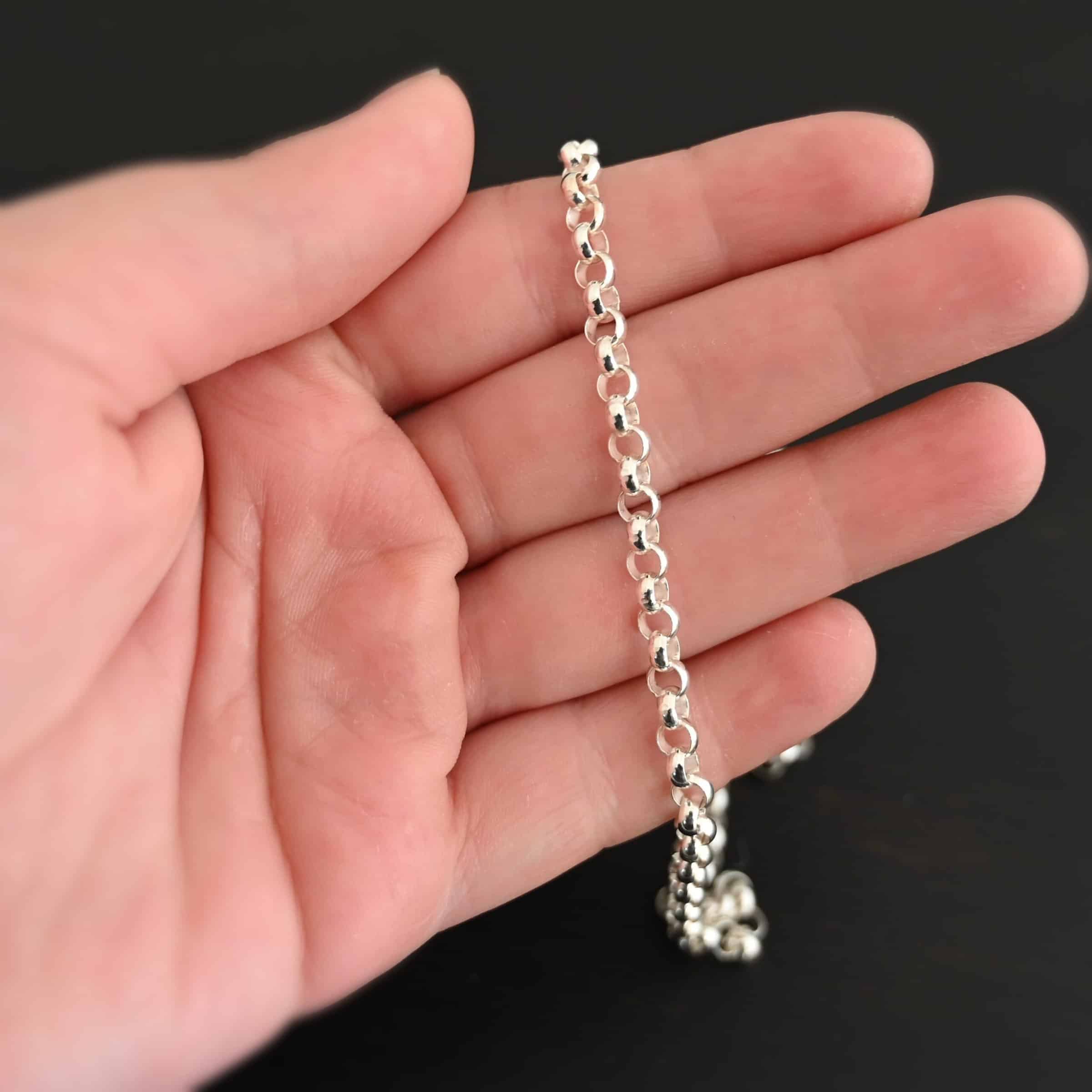 Shiny sterling silver Roxy Rolo Chain that is made with small circular links all connected together laying on a hand that is resting against a dark background