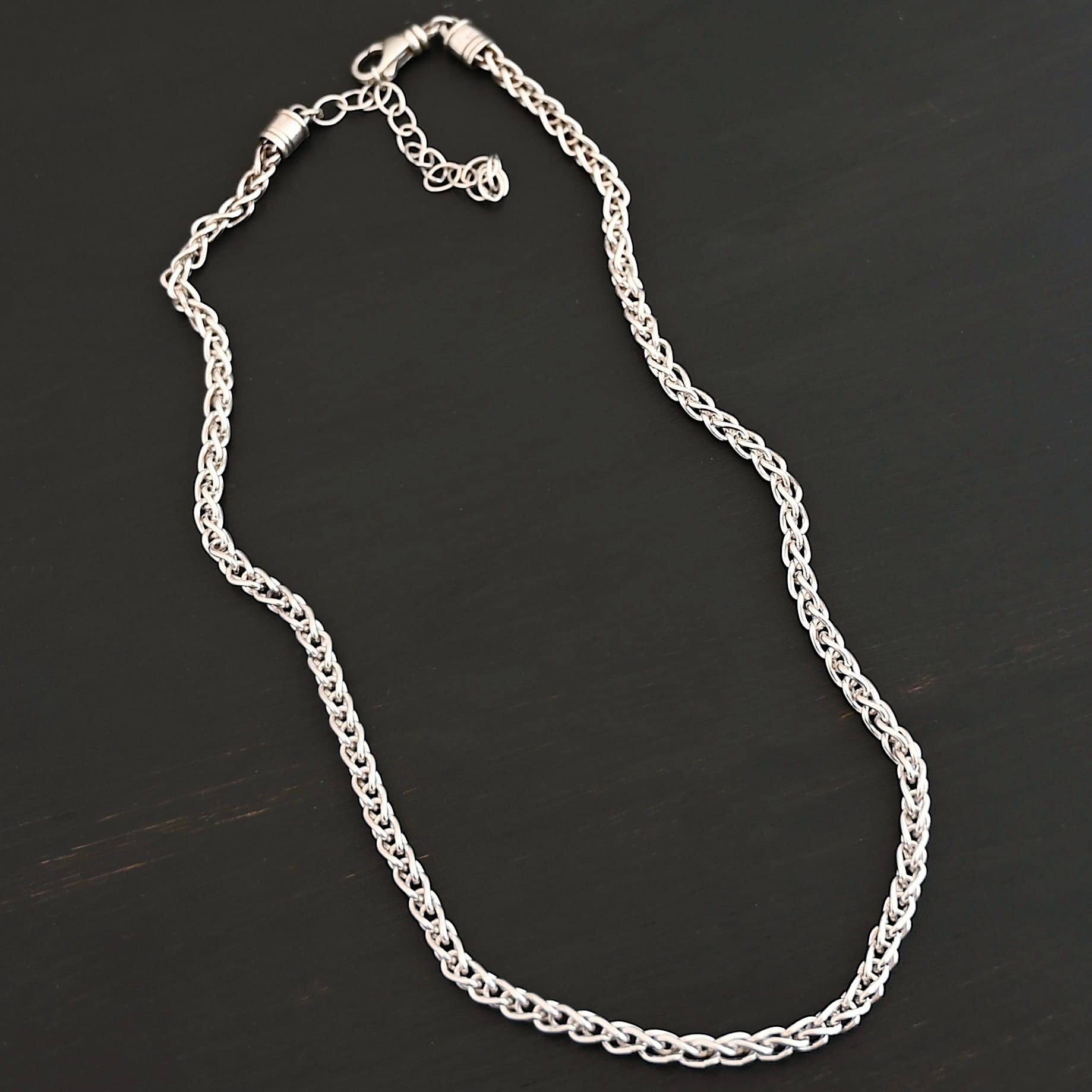 King Cobra Wheat Chain The "King Cobra" Wheat Chain. Chain is handmade out of sterling silver and woven together loosely. Each link is woven to another one and there are sterling silver end caps on each end of the chain. Chain has a lobster claw clasp and comes with a 3 inch extension. Chain is laying against a dark background. Chain is shown as shiny.