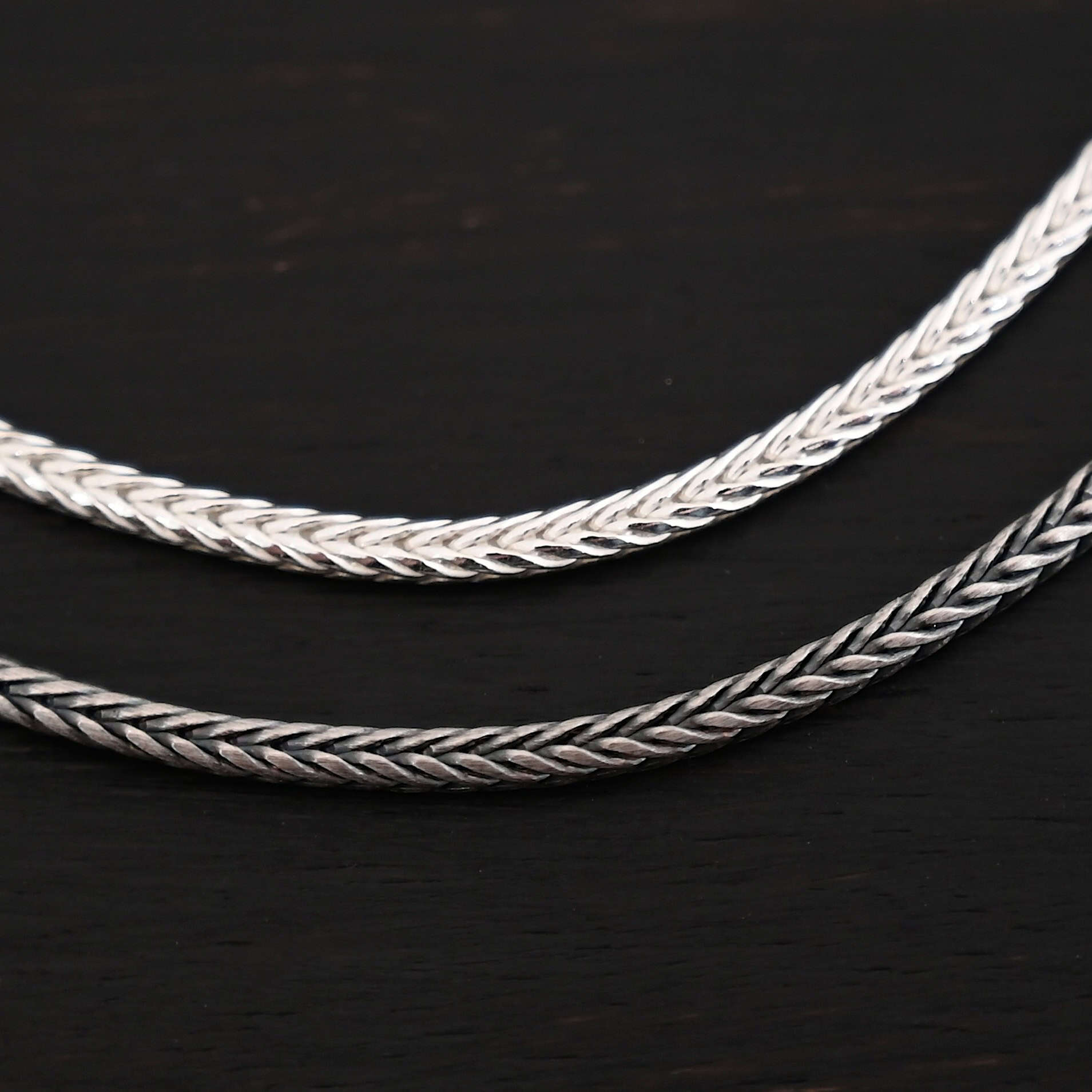 Close up of shiny & oxidized sterling silver Snake Foxtail Chain that is woven together tightly to form the chain that is resting against a dark background